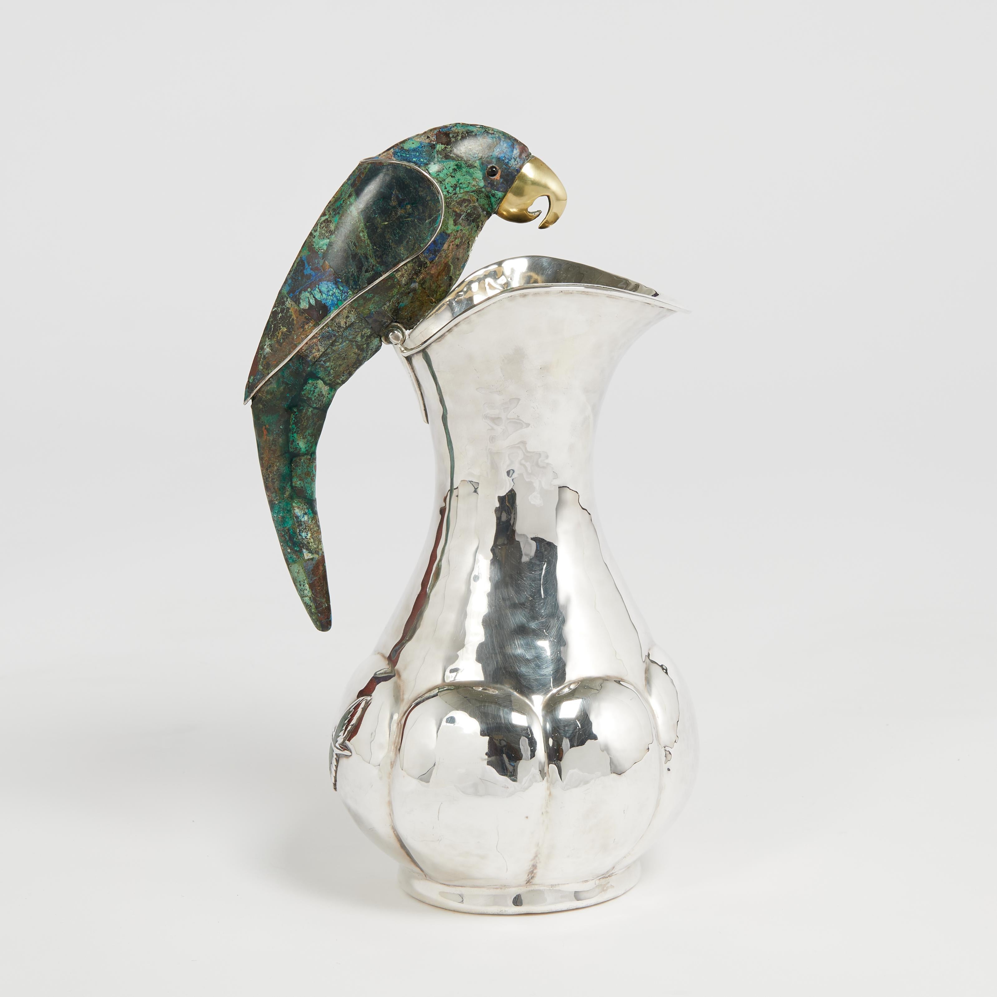 Standout mid century pitcher handcrafted in silver plate over hammered copper in modern form featuring a stone clad parrot as a handle and applied stone flying birds. Stamped on the bottom Los Castillo Mexico. 