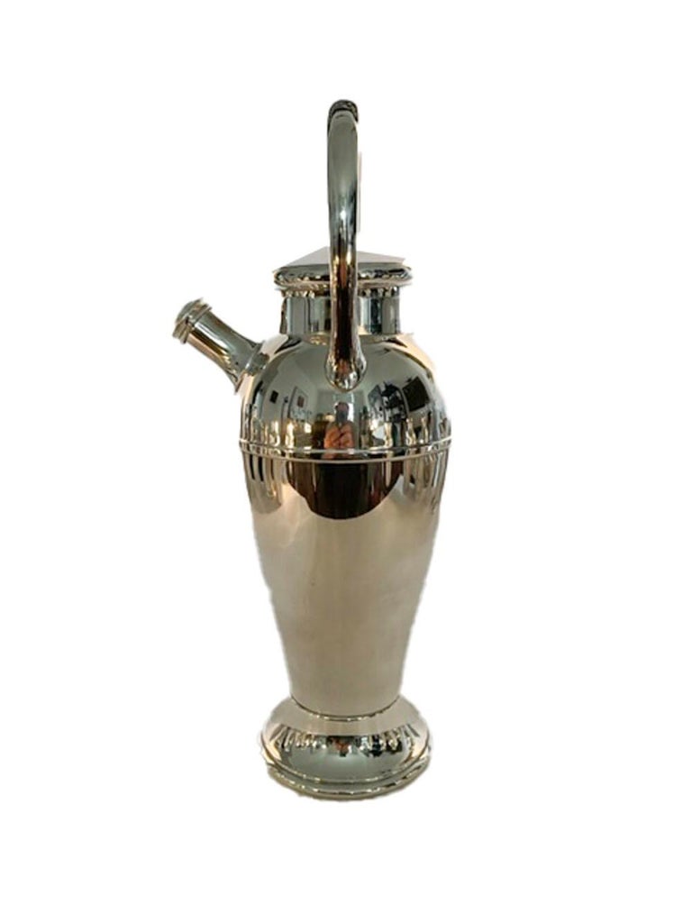 Silver plate, 48oz. cocktail shaker of urn-form on a raised foot, having a pour-spout with integral strainer and a large, fixed loop handle, for twisting, to spin the ingredients, or just hold on to the cover and foot and shake.