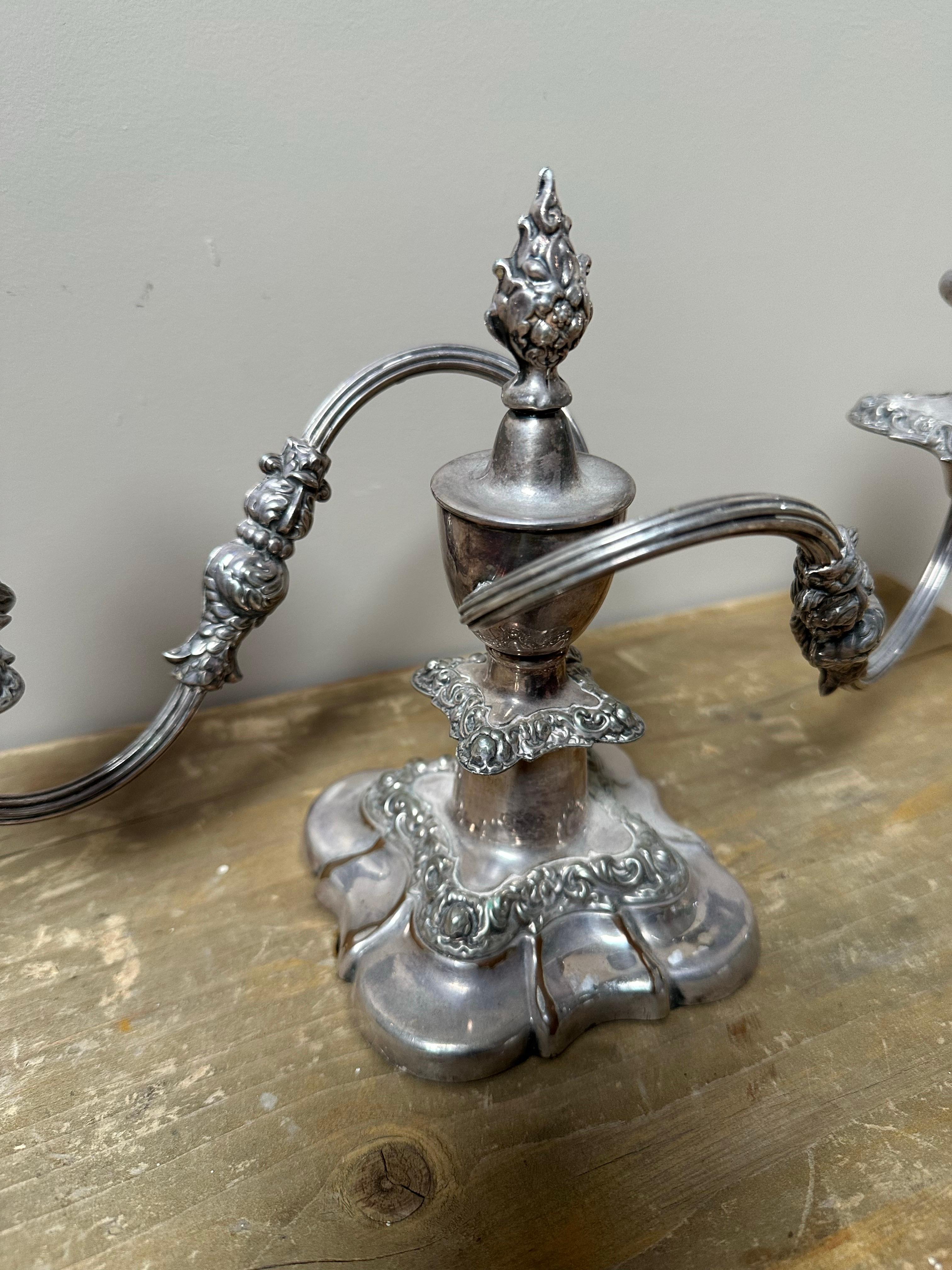 Porta un'eleganza senza tempo nel tuo spazio con questo candelabro vintage a due bracci placcato in argento, un portacandele decorativo di ottima fattura progettato per contenere due candele a cero. Probabilmente influenzato dal design dell'Art