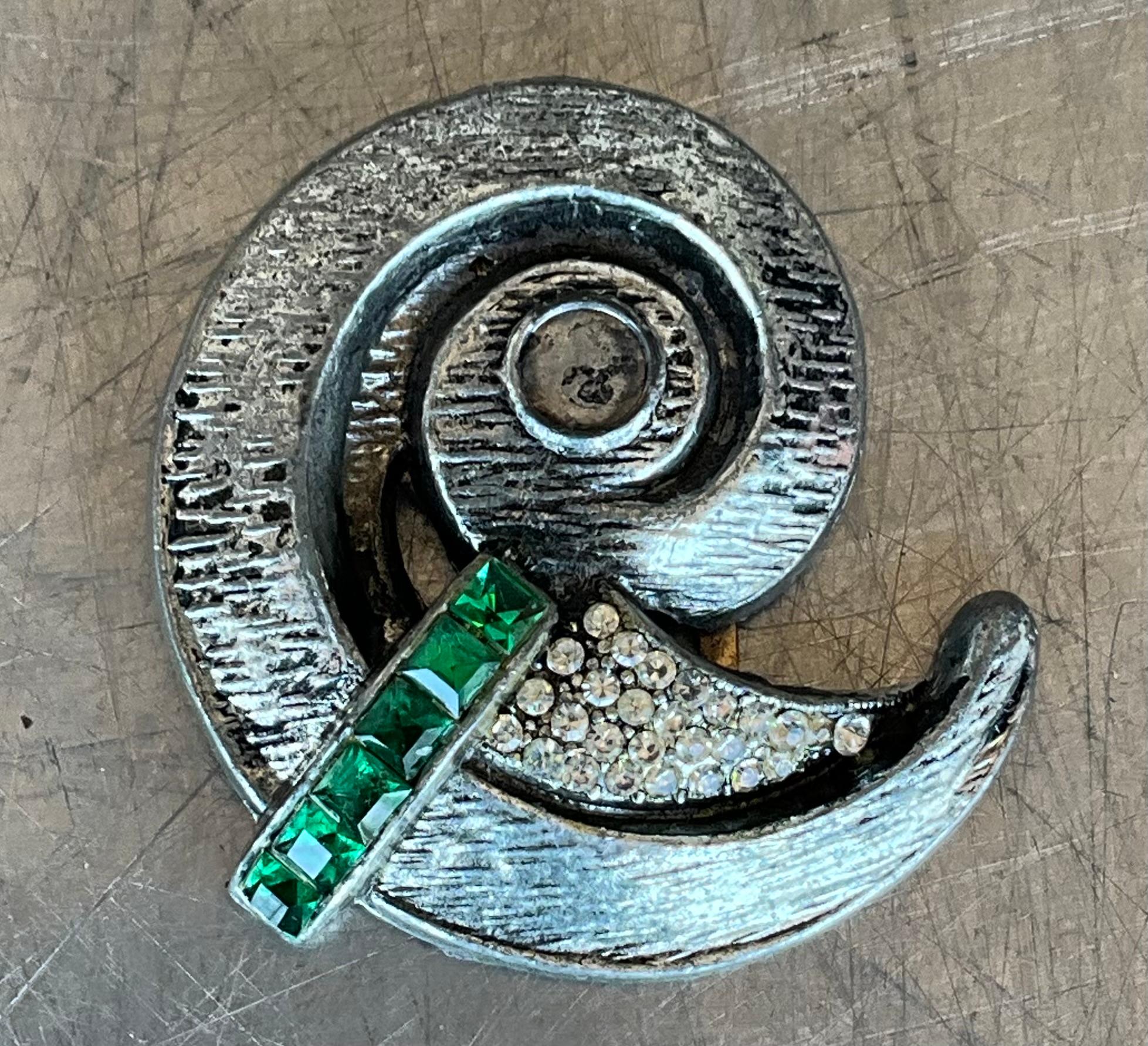 Una spilla vintage a spirale in argento con dettagli verdi sembra un gioiello bello e intrigante. La combinazione tra l'argento, intramontabile ed elegante, e gli accenti verdi (probabilmente sotto forma di smalto, pietre preziose o strass) crea un