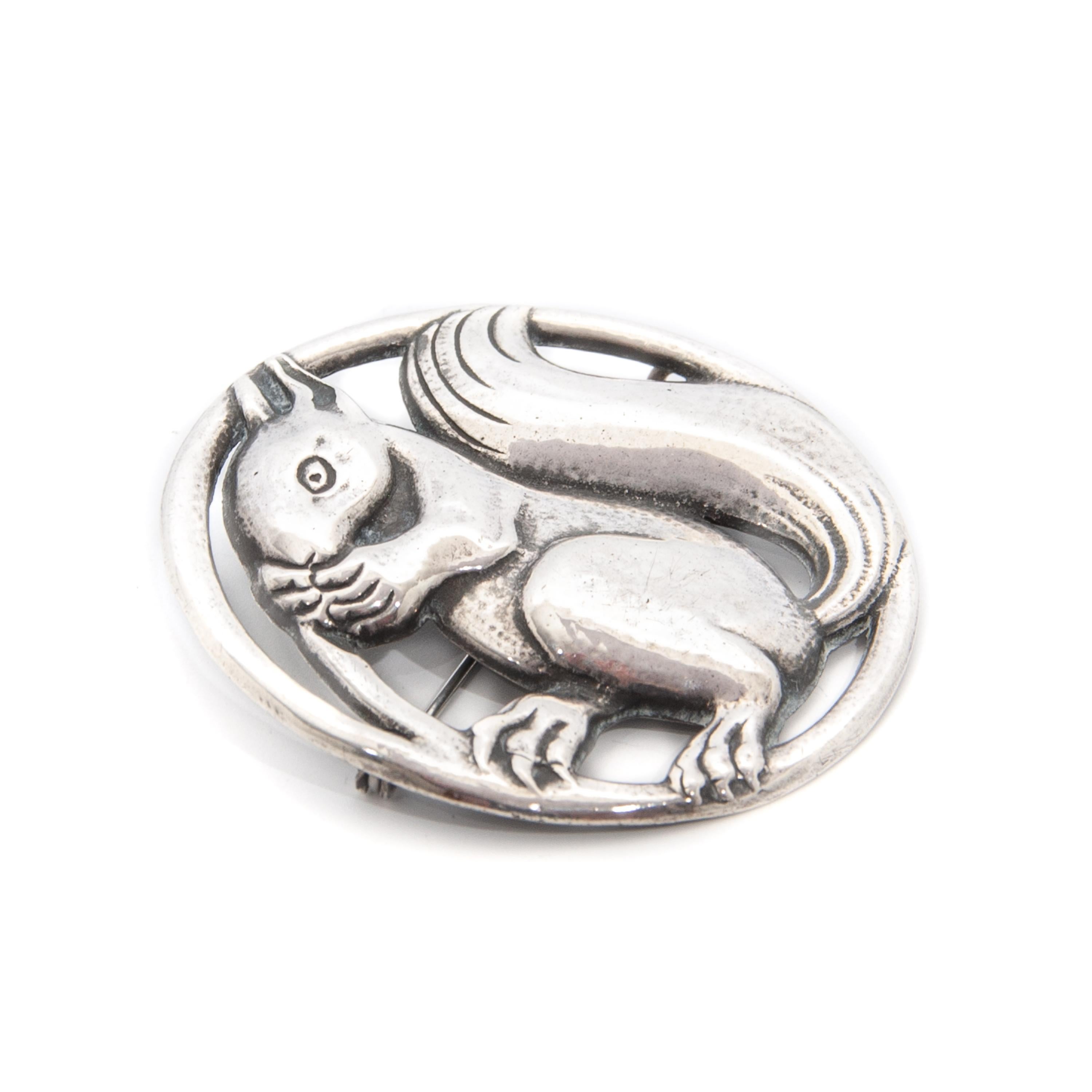 A lovely vintage silver round squirrel brooch. The brooch is made of polished silver and beautifully stylized, while the line engravings of the cute animal have a natural patina. The squirrel is resting on a branch and eating an acorn. At the back