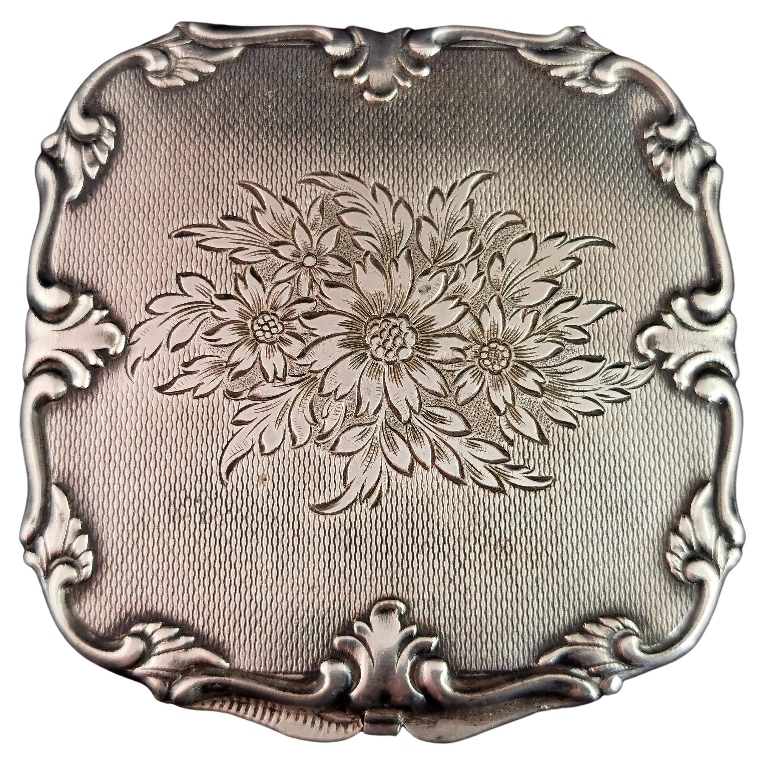 A gorgeous vintage mid century, silver tone metal powder compact.

It has a slightly wavy edge with a slightly raised repousse rim, engine turned design front and back with a floral motif to the top.

Inside it has an internal compartment for powder