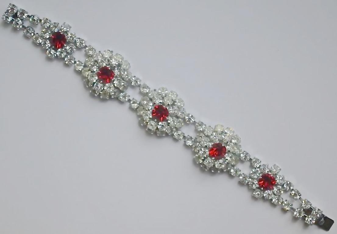 Stupendo braccialetto in argento con bellissimi strass rossi rubino e trasparenti, circa anni '50. Ci sono tre gruppi di strass trasparenti, ciascuno con uno strass rosso centrale, e due gruppi più piccoli. La lunghezza è di 18,6 cm, mentre i