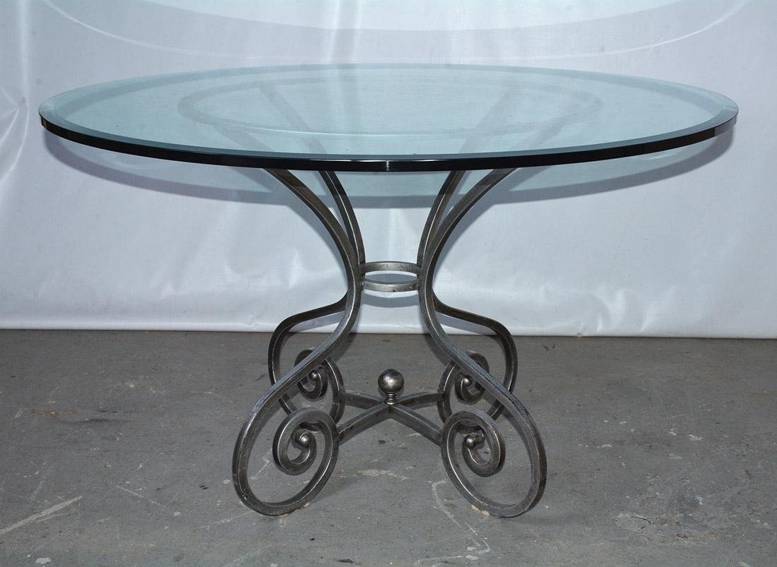 Der Tisch ist aus silberfarbenem Schmiedeeisen im modernen Bistro-Stil gefertigt und mit einer runden Glasplatte versehen. Die Basis des Vintage-Tisches besteht aus vier Volutenbeinen, die durch zwei gekreuzte Strecker und ein rundes Stück gesichert