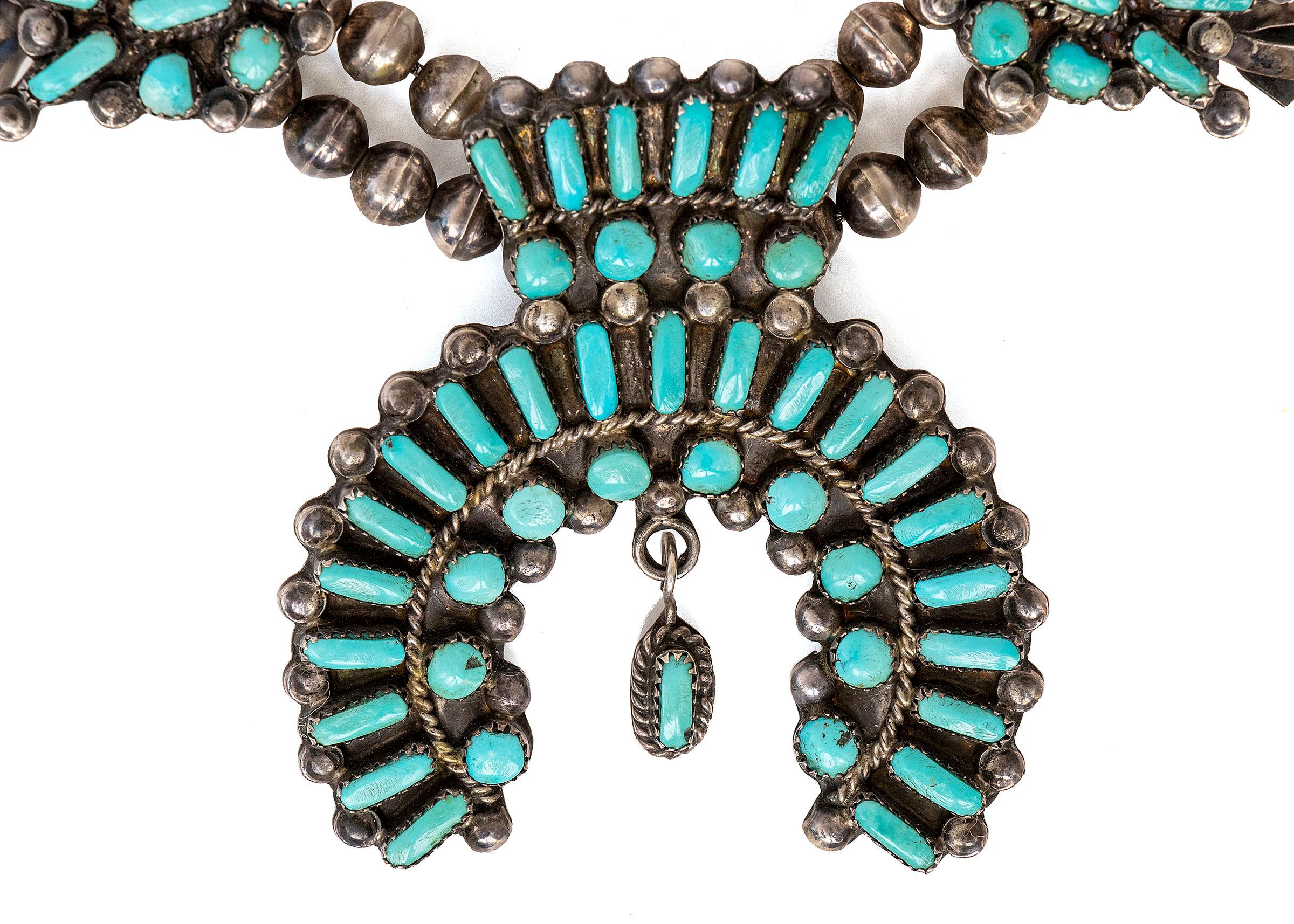 Vintage Zuni Squash Blossom necklace with 12 squash blossoms and a horse shoe Naja. Silver with turquoise stones. Dimensions measure the necklace is 15½ inches in length.

Necklace is clean and in very good vintage condition

Expedited shipping is