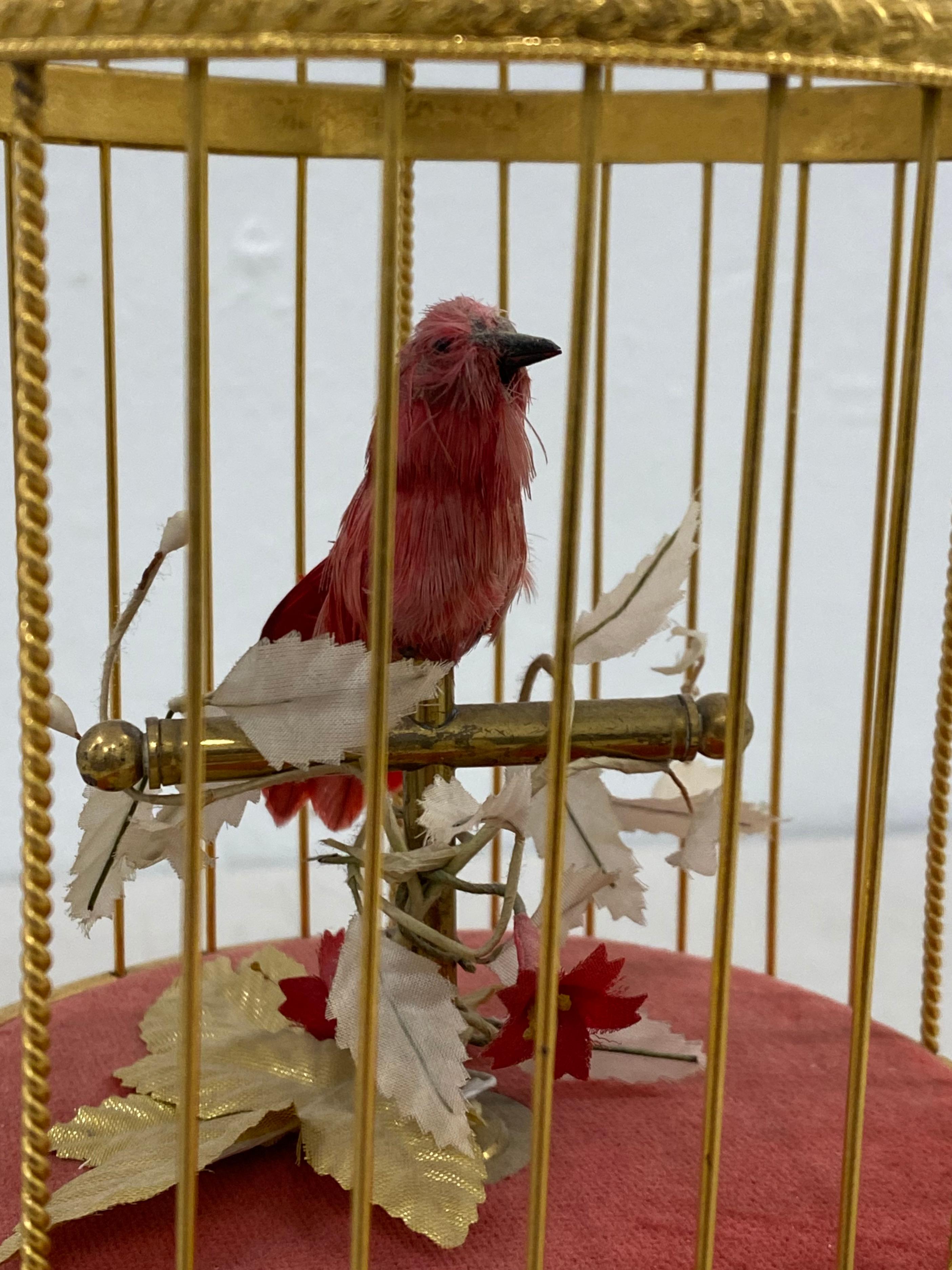 Vintage singing bird in a gilded cage automaton C.1930s

This charming little red bid sings when you wind her up

The mechanics are in working condition and the bird chirps away and her body moves a bit

The bird, plants and red fabric show
