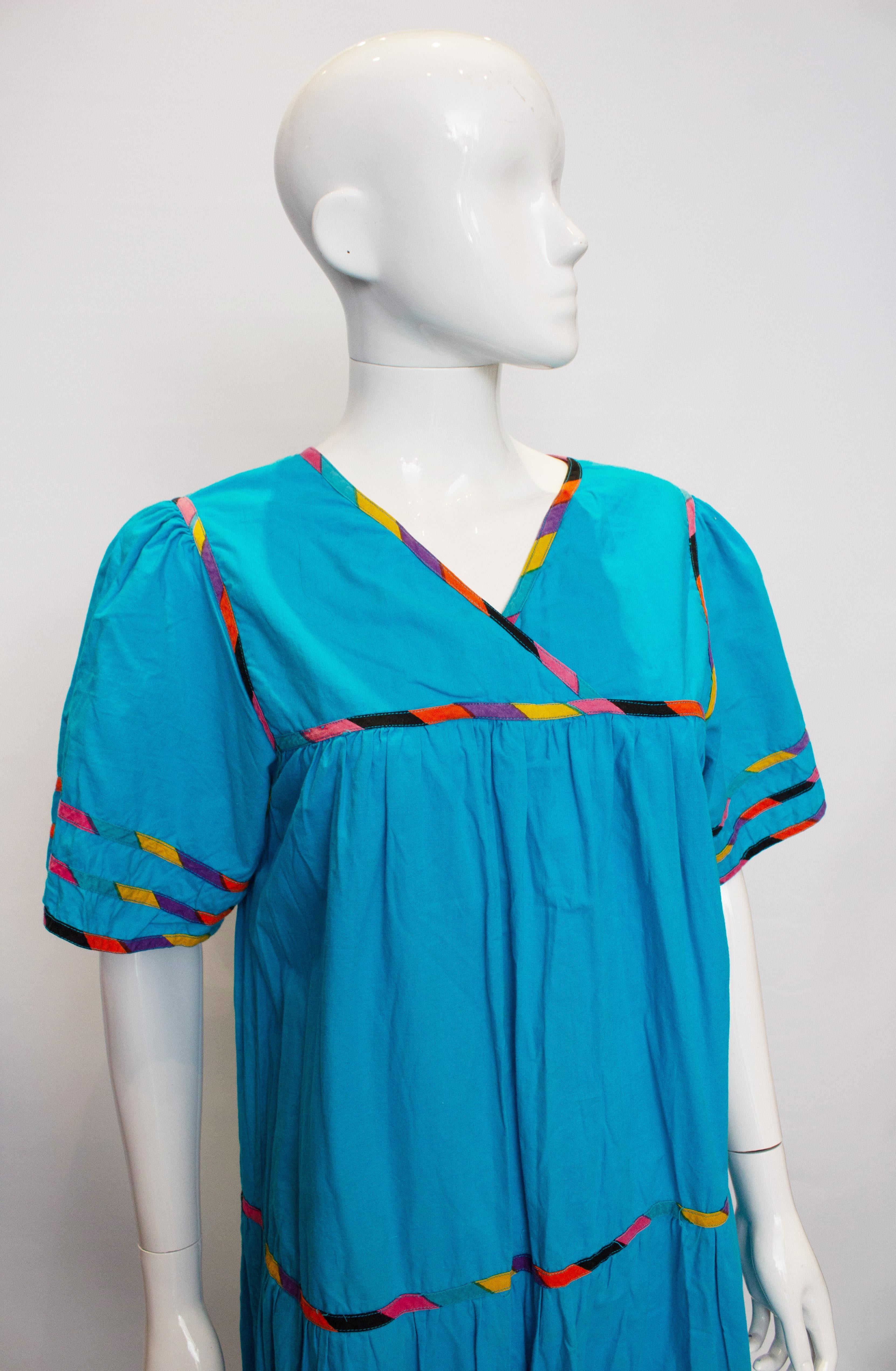 A fun vintage dress for summer. In a bright turquoise with a multi colour trim on the neckline, sleaves and tiers of fabric. The dress has a pocket on either side.