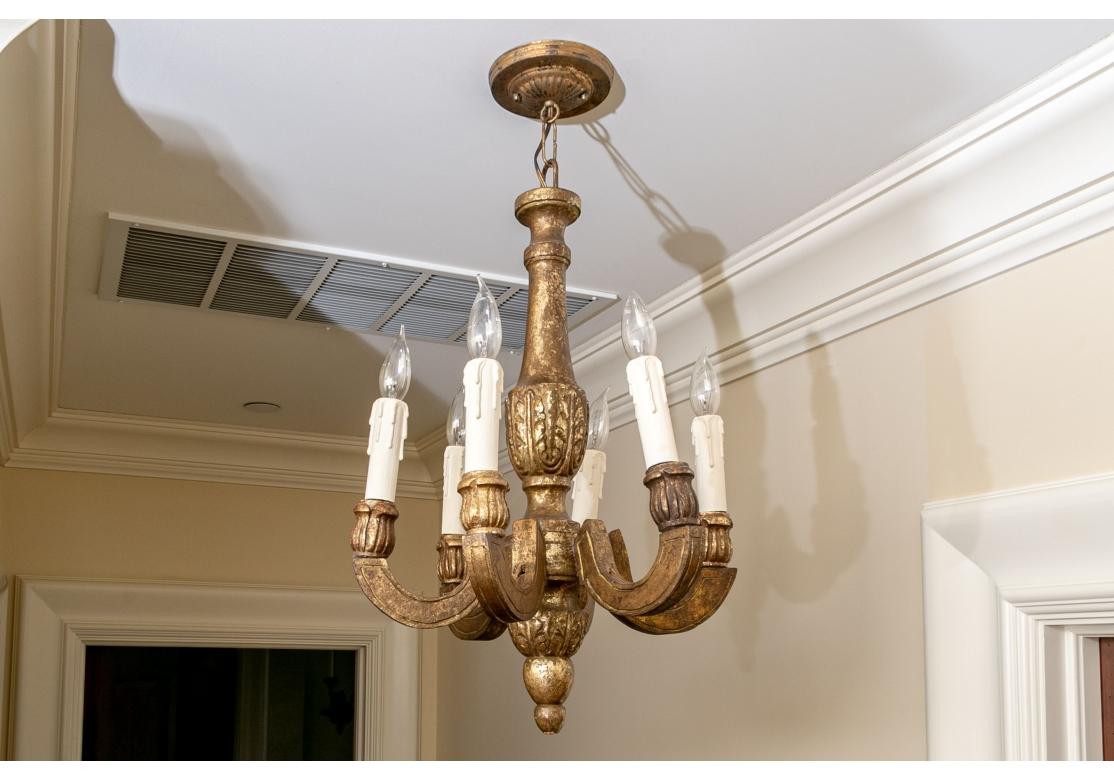 Lustre à six lumières en bois sculpté et doré, finement travaillé et élégant, en finition antiquaire. L'étalon de forme balustre avec une haute base feuillue. Six lampes carrées et incurvées sont décorées de larges douilles feuillues sculptées pour