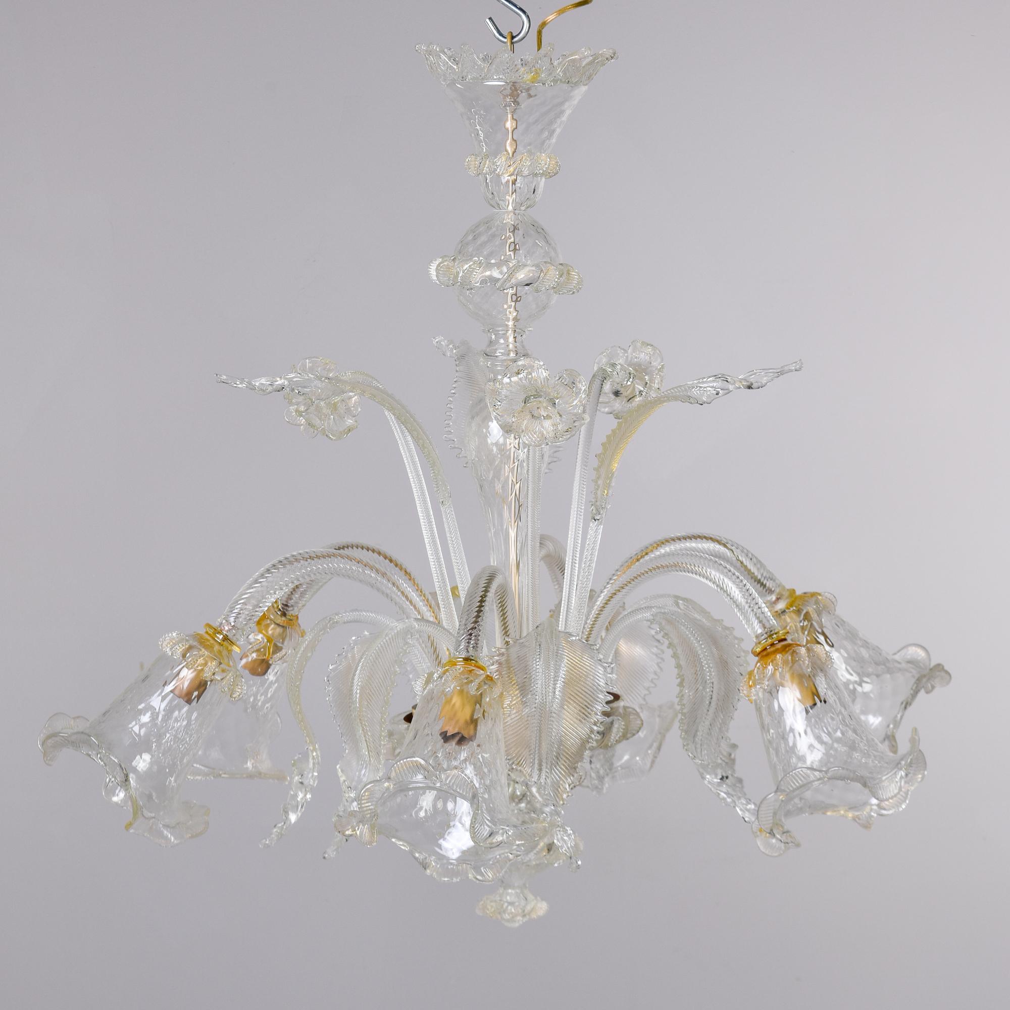 Circa 1980s Murano chandelier in clear glass with gold inclusions. This fixture has six arms with standard-sized sockets that have been rewired for US electrical standards. Upper portion of fixture has mouth blown glass curled leaves, daffodils.