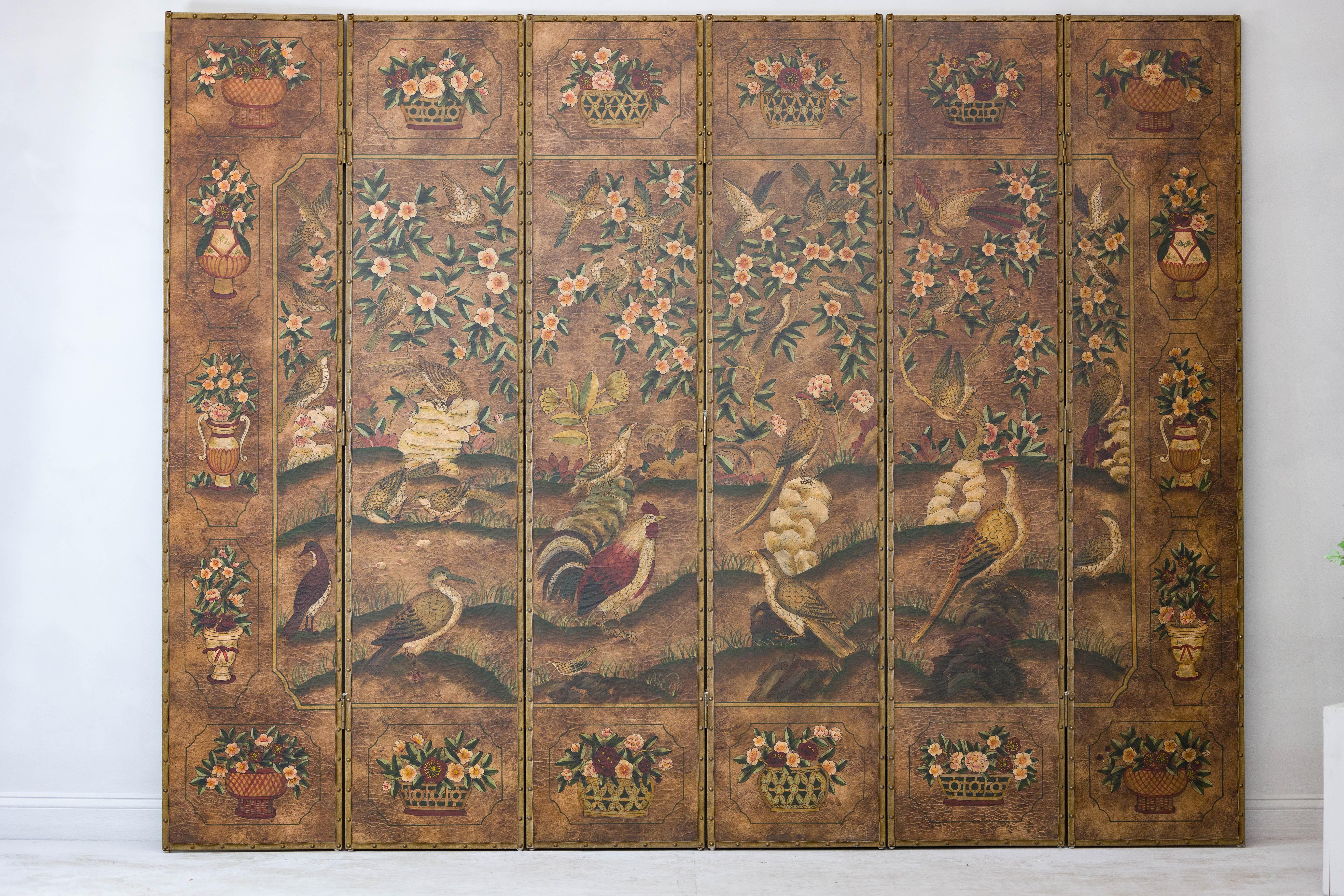 This vintage six-panel screen, crafted from hand-painted leather, showcases an intricate scene of birds, roosters, and blossoming branches, framed by brass nailhead trim. Hand-painted birds and blooming branches spread across six panels of warm,