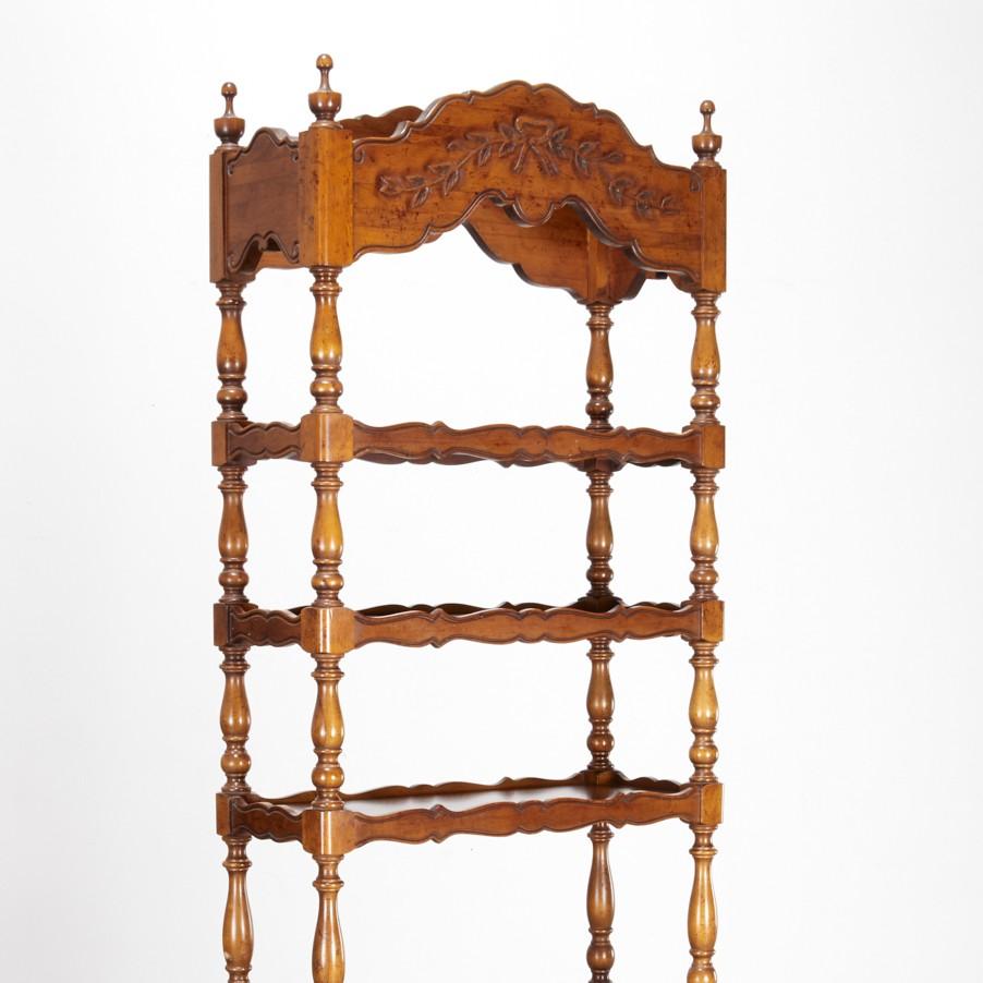 Elegante étagère a sei piani in noce di gusto provinciale francese, con supporti a balaustro torniti e ripiani smerlati intagliati. Lo stemma e il grembiule inferiore sono decorati con nastri e motivi rinceau, che aggiungono un grazioso tocco