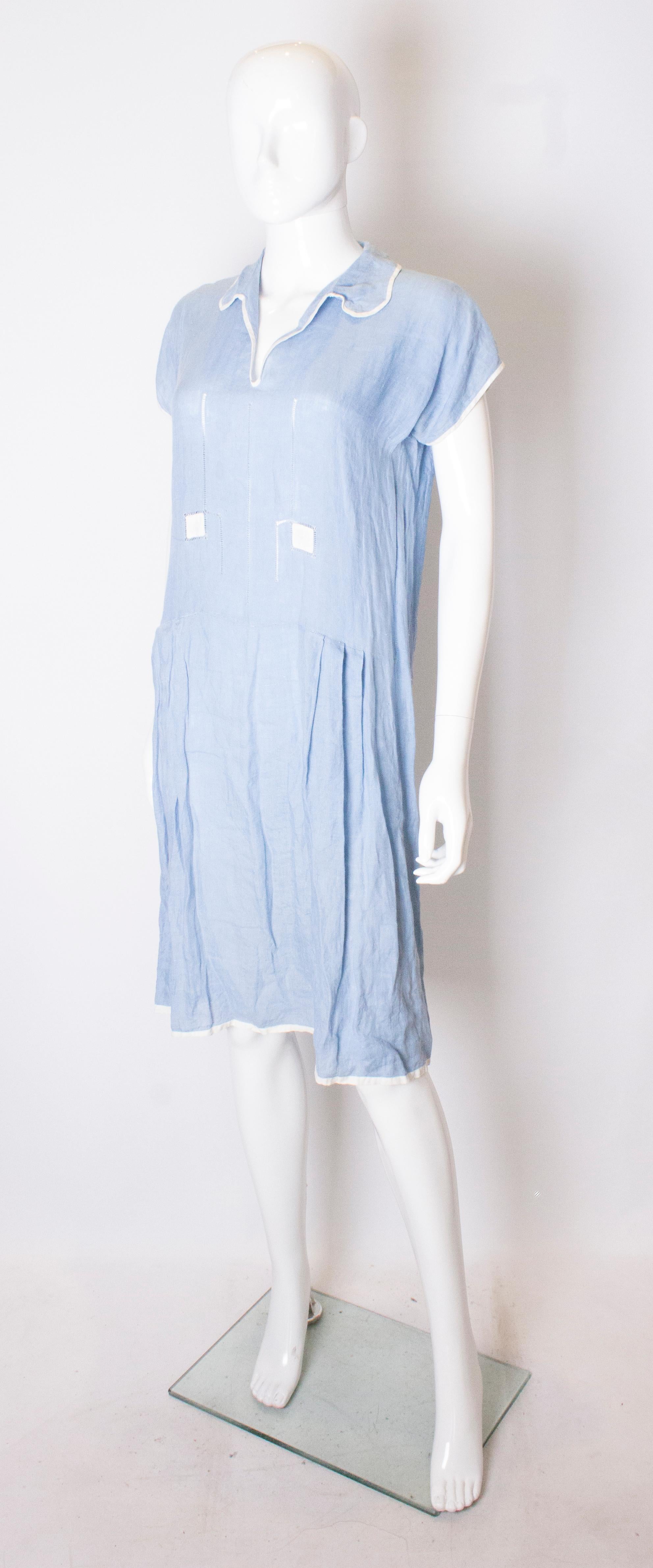 A pretty summer dress from the 1920s. The dress is in a sky blue linen with white piping. The dress has a v neckline and gathering at hip leval.