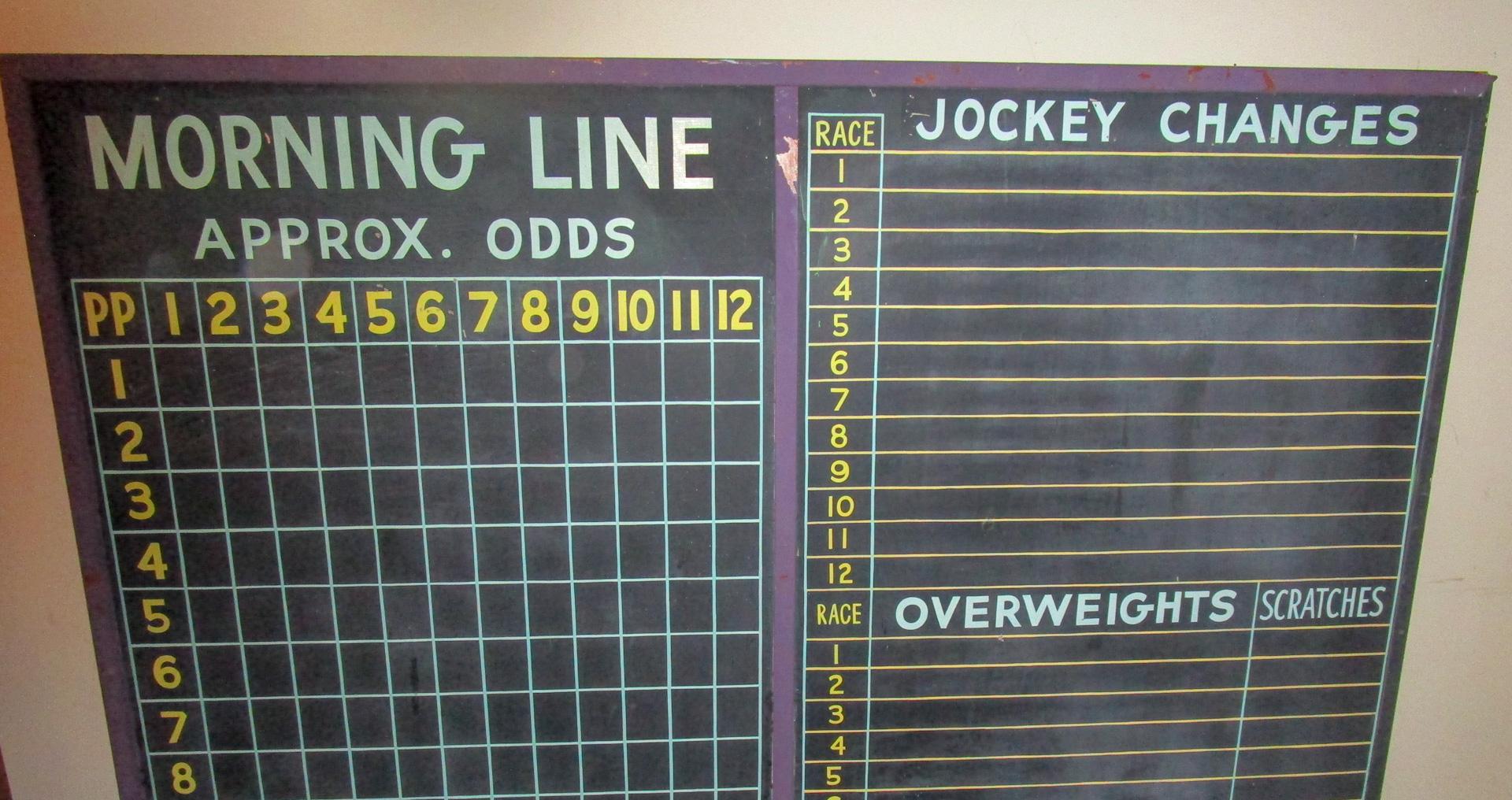 This very large horse racing slate chalk board calculates the morning line up with the approximate odds, jockey changes, overweights and scratches for twelve races. Framed in a painted purple wooden framework, it is the perfect addition to your game
