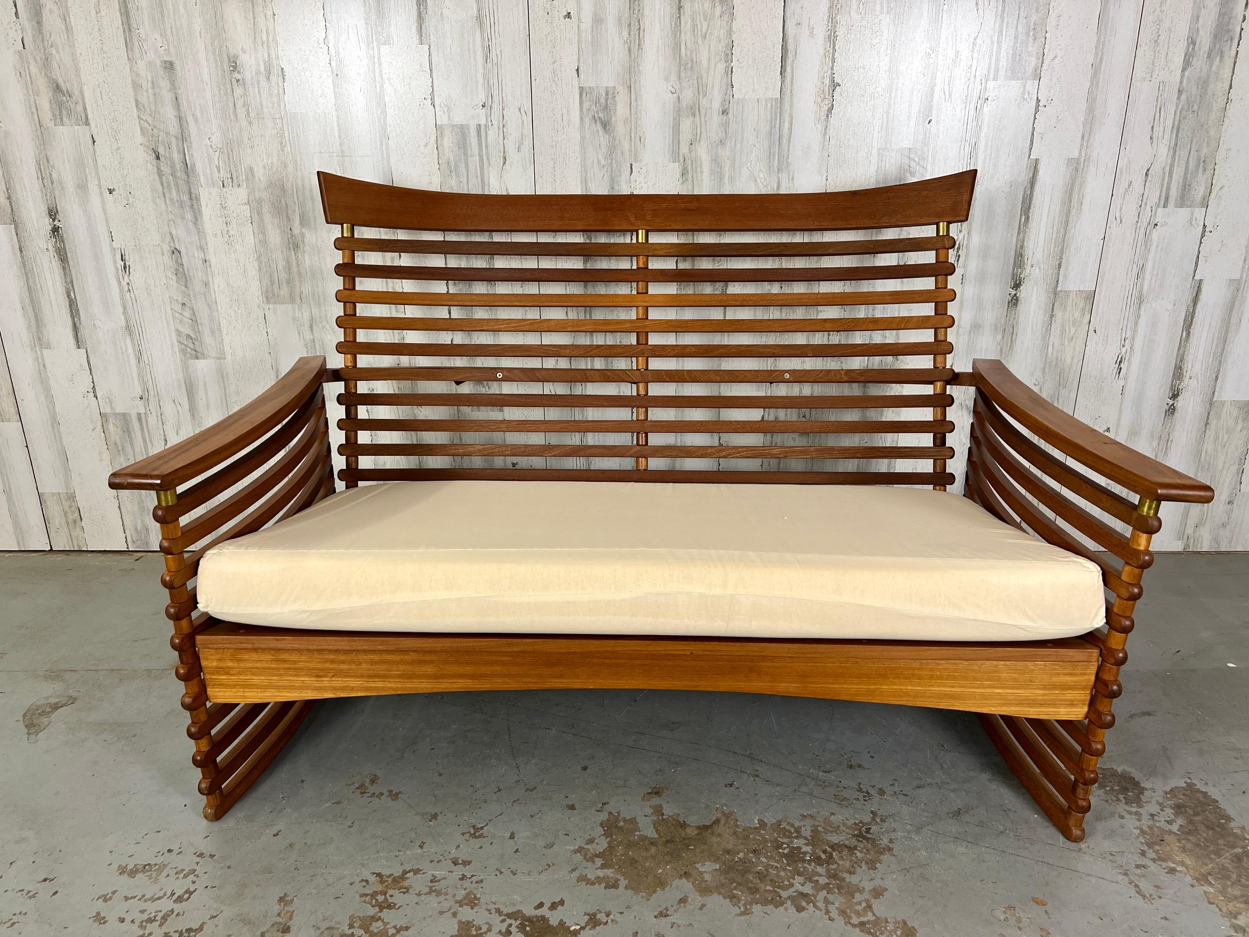 Solid Teak slats with brass accents. The sides are curved with a nice angle on the back. This settee is very sturdy and very comfortable for long term sitting. 
New upholstery is required.