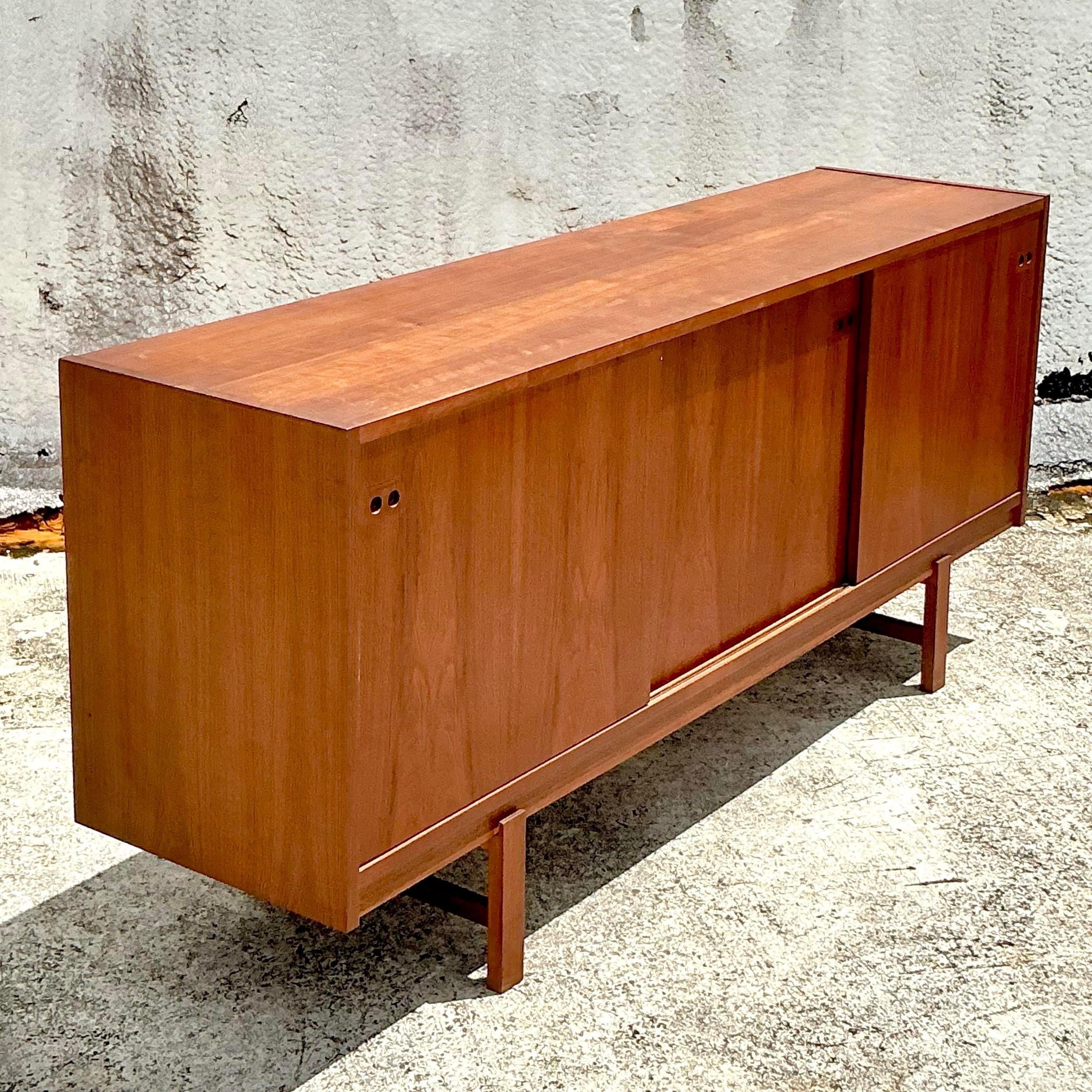 This Mid-Century Modern teak credenza, inspired by Kofod Larsen, features sleek sliding doors and clean lines. A timeless piece that brings both style and functionality to any modern space. Ideal for stylish storage or as a statement piece.