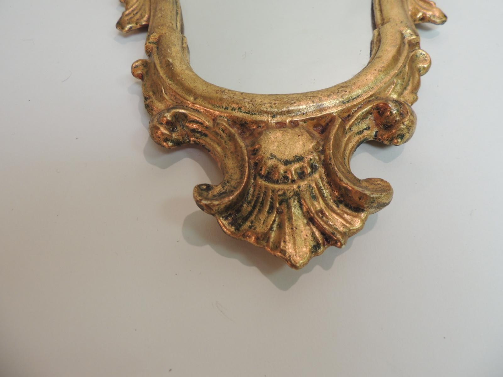 Small vintage ornate wood carved Italian gold leaf wall mirror. Serpentine lines with a stylized feathers crest on top and bottom. Original made by hand label still in the back. Back with red velvet paper. Hanging hook.
Italy 1960s.
Measures: 9.5