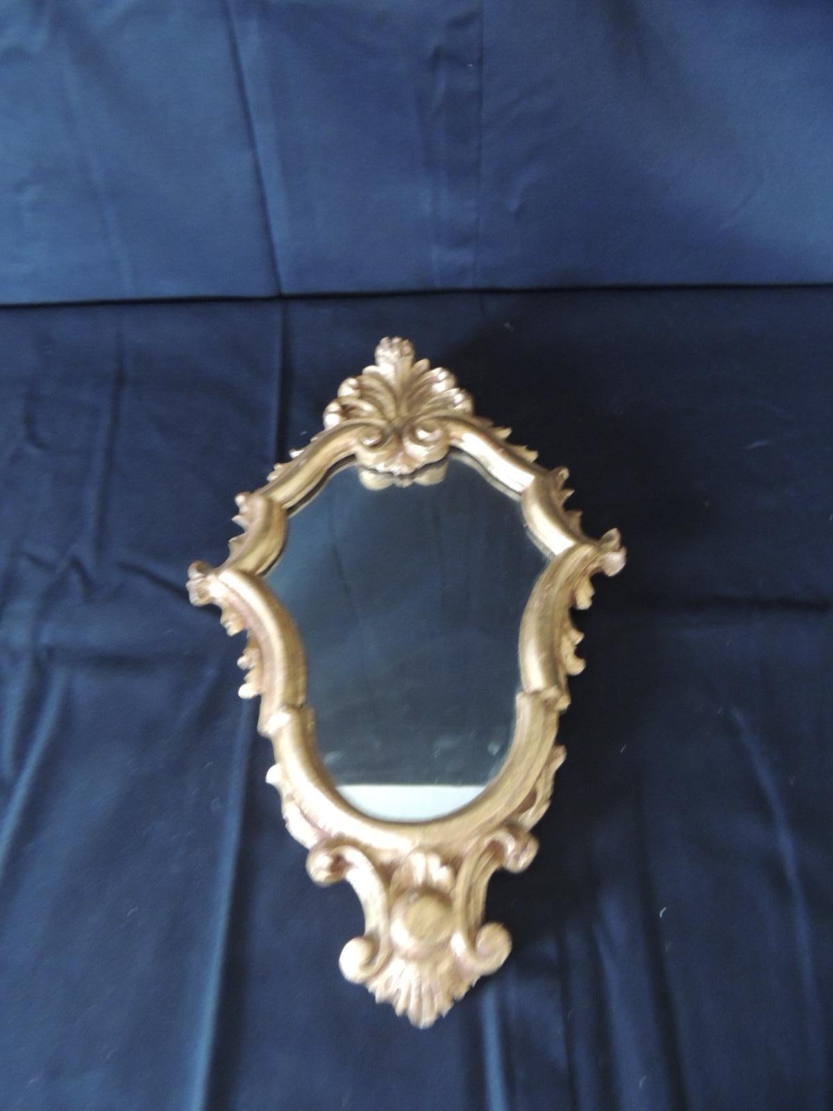 Small vintage ornate wood carved Italian gold leaf wall mirror. Serpentine lines with a stylized feathers crest on top and bottom. 
Original made by hand, Hanging hook.
Italy 1960s.
Measures: 8.5