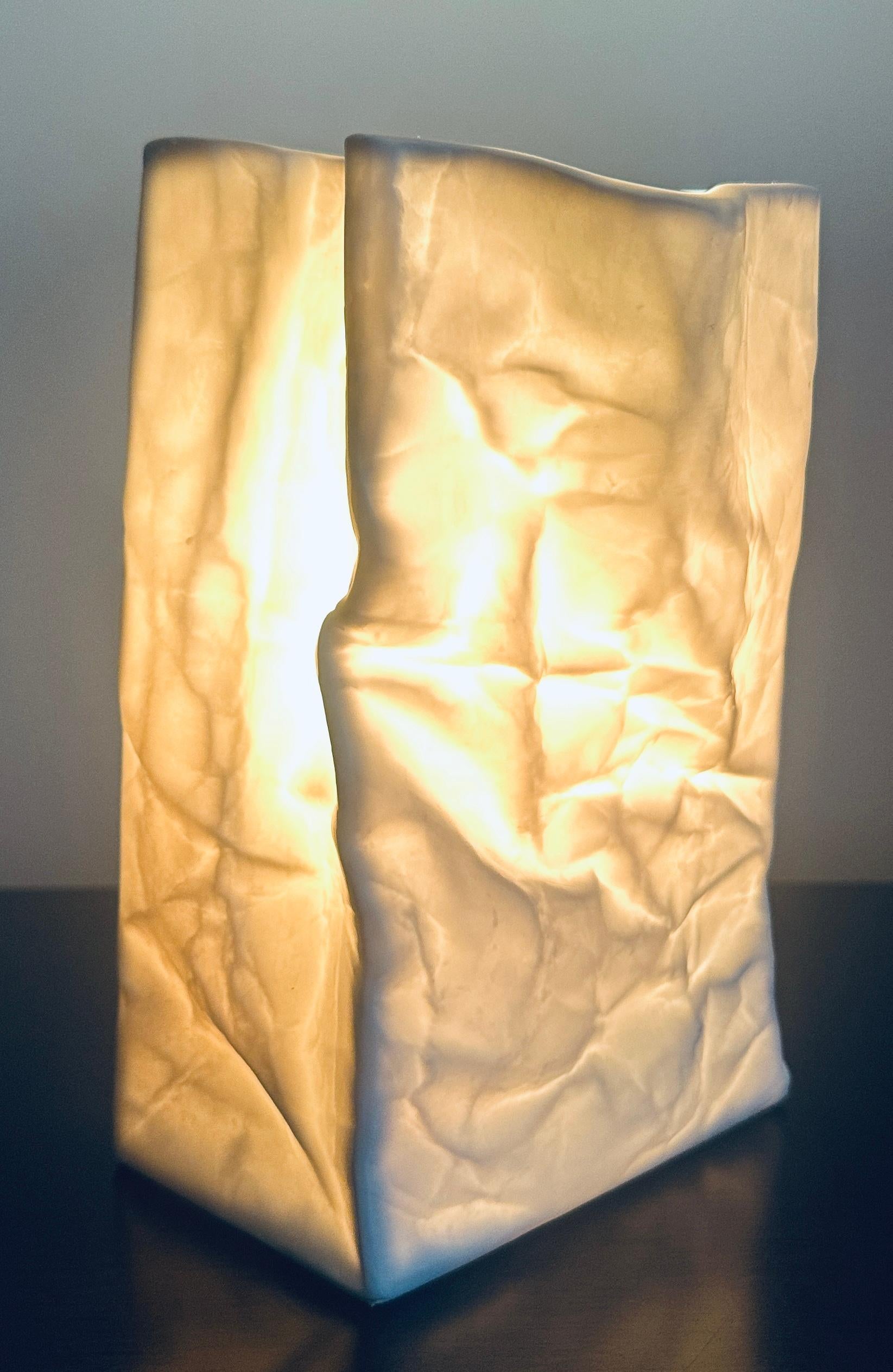 Lampada da tavolo in ceramica francese anni '70 in bisquit bianco opaco con sacchetto di carta stropicciato attribuita a Sompex e vasi simili disegnati da Tapio Wirkkala per Rosenthal.

La forma scultorea accartocciata e molto realistica del
