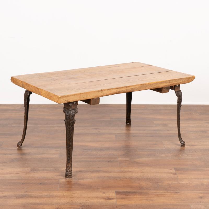 This rustic coffee table may also serve as a unique side table, thanks to the vintage iron legs that accent the warm patina of the worn pine top. Typical age-related separation of the planks, scratches, dings, cracks, old (dried) wormholes and