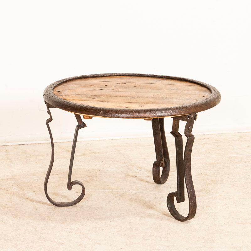 The round wooden top is a great contrast to the wrought-iron base of this vintage small coffee or side table. It has been restored and waxed, bringing out the warm patina of both wood and iron. Any cracks, knicks or scratches are age-related and do