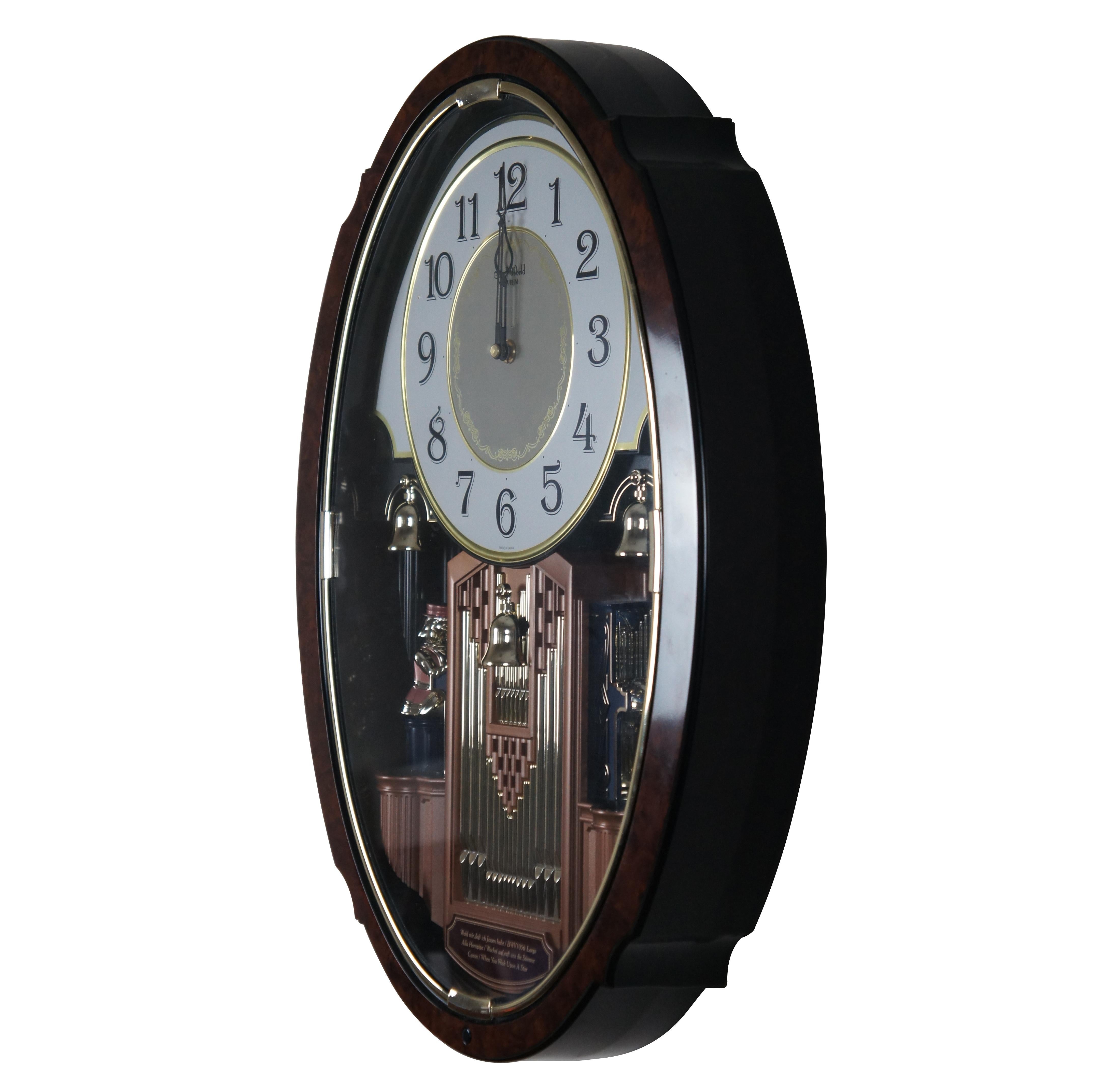 Late 20th century Rhythm Small World, battery operated, musical animated wall clock. Made in Japan. Features an oval plastic case finished with a burl wood veneer, with a white and gold face over a gold, copper and blue painted pipe organ and bells,