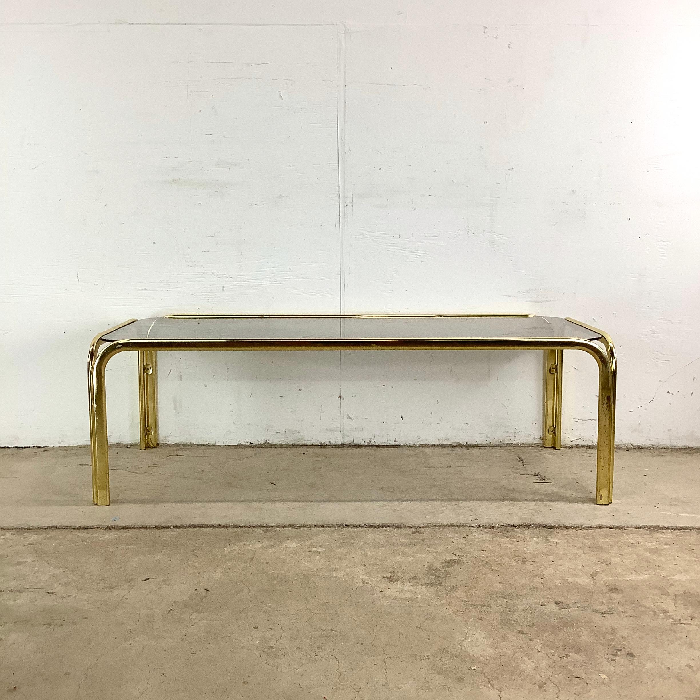 Cette table basse en laiton et en verre incarne le glamour absolu des années 1970 avec une retenue raffinée qui résonne encore aujourd'hui. Le cadre rectangulaire, fini en laiton brillant, fournit une base structurée pour le plateau en verre