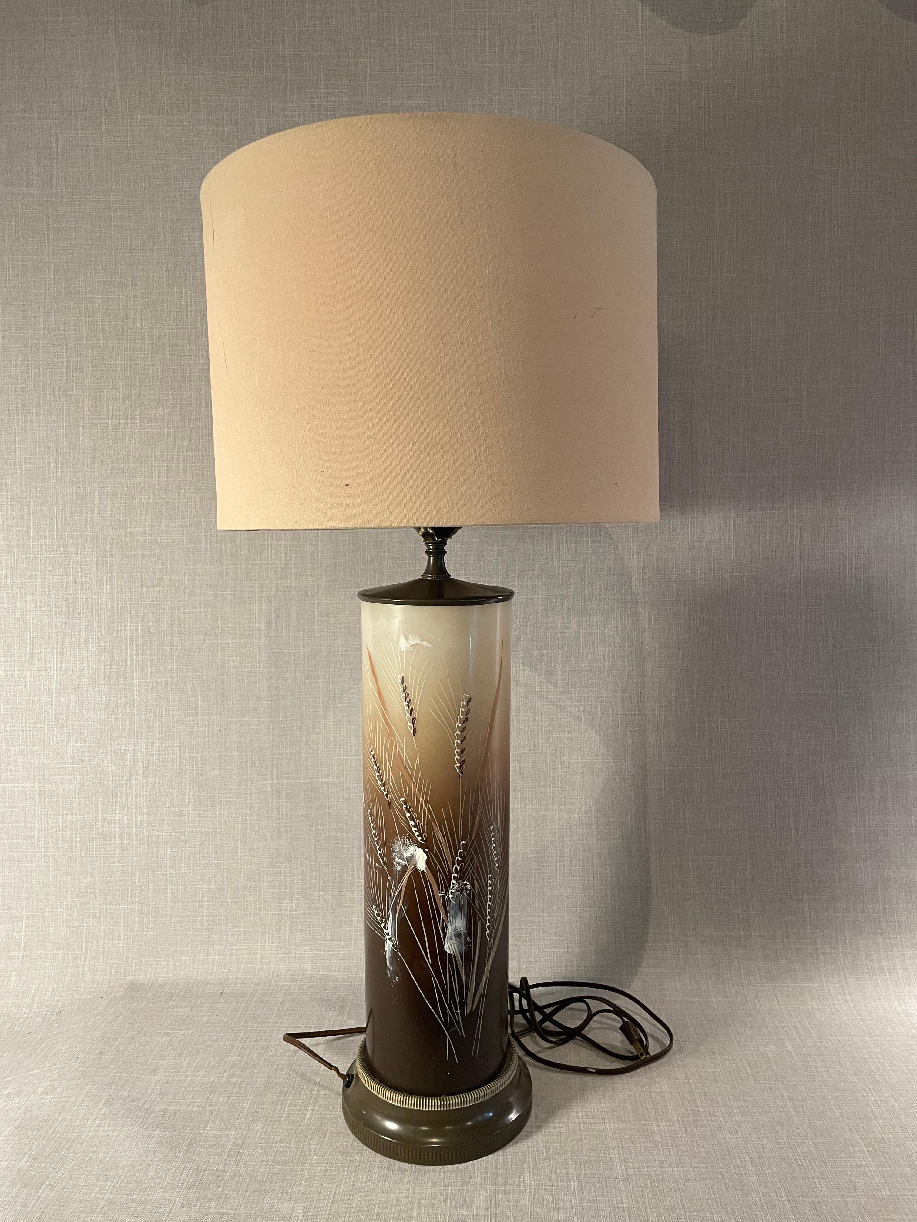 Diese charmante Vintage-Tischleuchte fängt den zeitlosen Reiz des Designs aus der Mitte des 20. Jahrhunderts ein, indem sie natürliche Motive mit eleganter Handwerkskunst verbindet. Die Leuchte verfügt über einen hohen zylindrischen Sockel aus