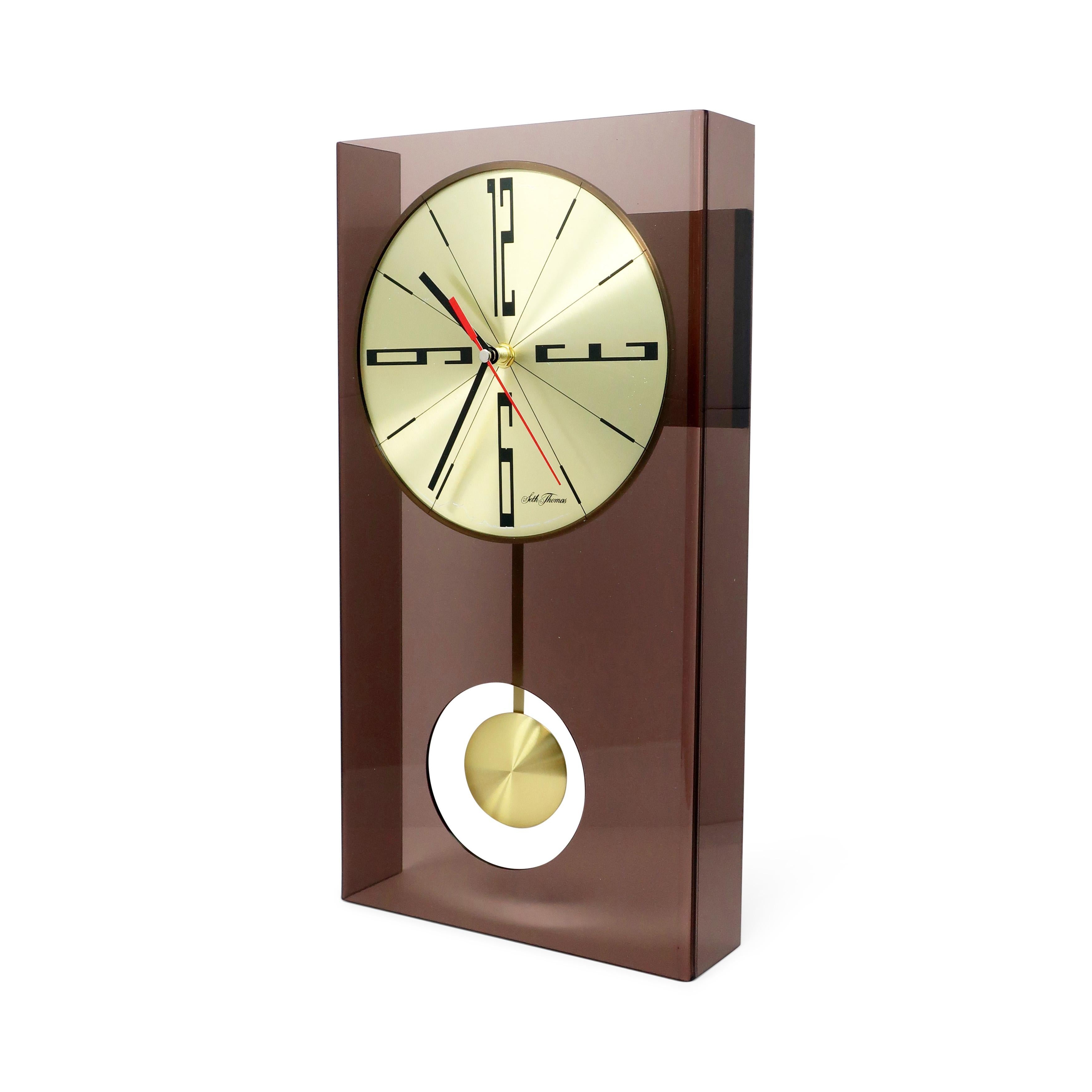 A mid-century modern smoked lucite wall clock by Seth Thomas, likely from the 1970s.  The clock has a brass face and pendulum, black and red hands, and black numbers.

In good vintage condition with wear consistent with age and use.  Marked 