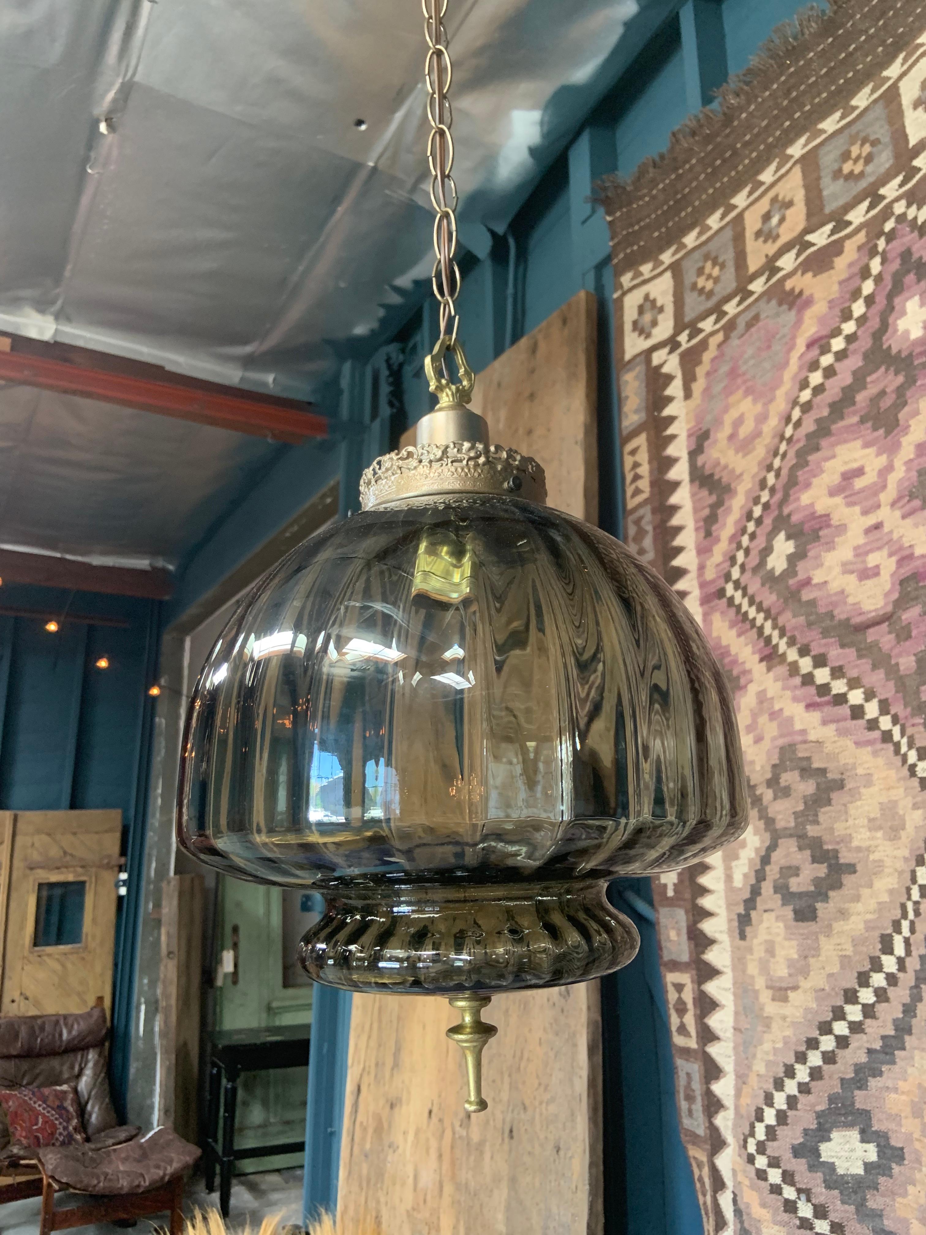 This uniquely designed glass hanging pendant has vertical ridges and a brass base with Victorian style accents. This combination of smokey glass and aged brass hardware creates a gorgeous mood in any space.