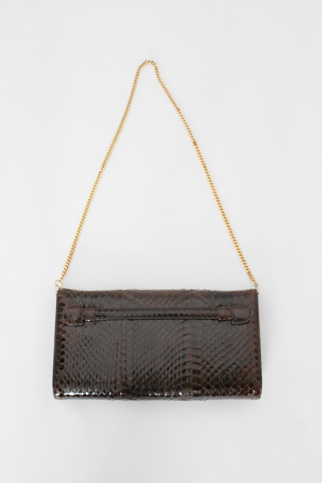 This presented high-quality chocolate brown snake skin handbag shows a golden brass chain and also fittings made of brass. 
The linen was made of brown suede leather and has an inside pocket. For closing the brown handbag it features a pressure
