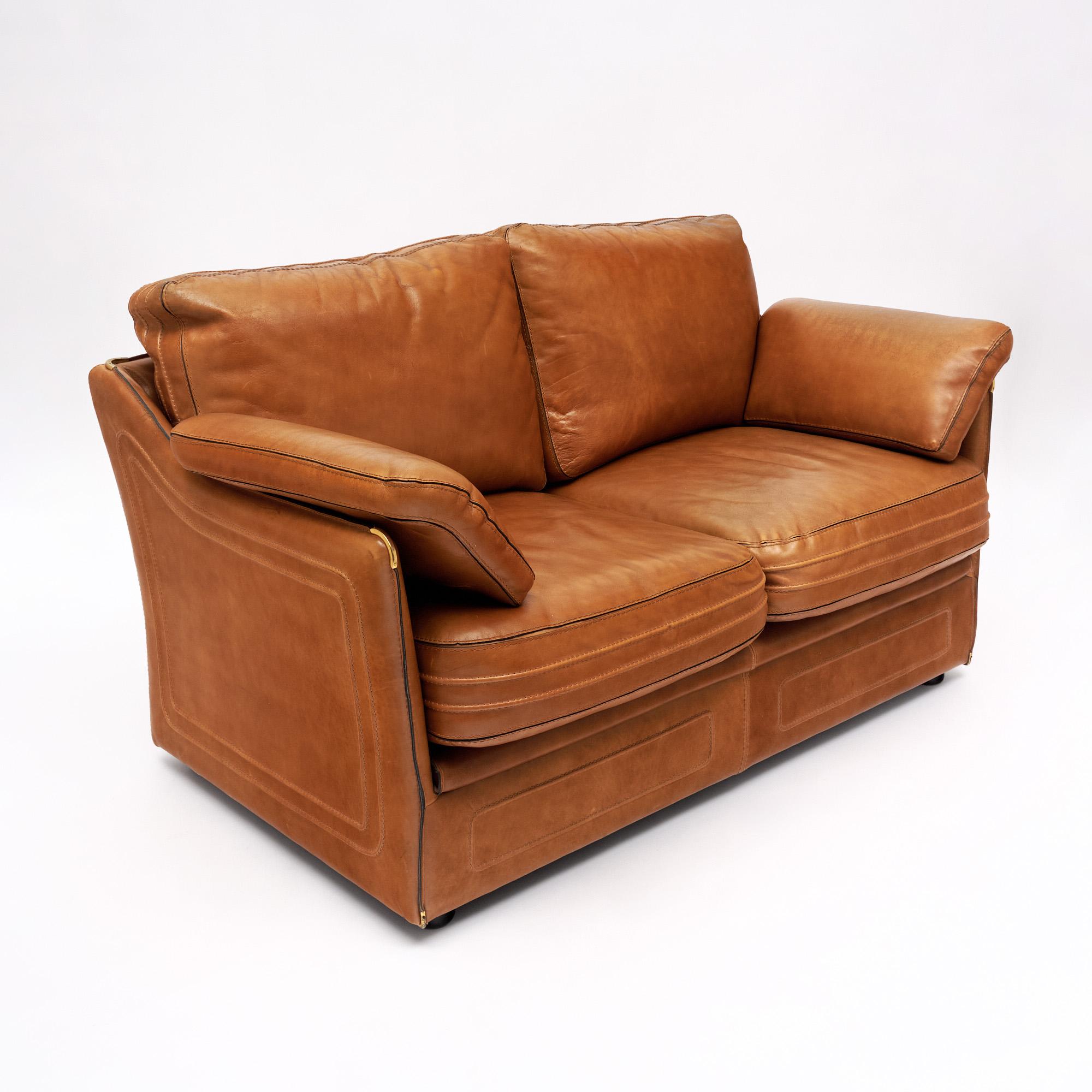 Sofa from mid-century France by renowned furniture brand Roche Bobois. This piece is made of camel colored leather with saddle stitching and a very comfortable cushion seat. Brass embellishments adorn the leather corners. We love the quality leather