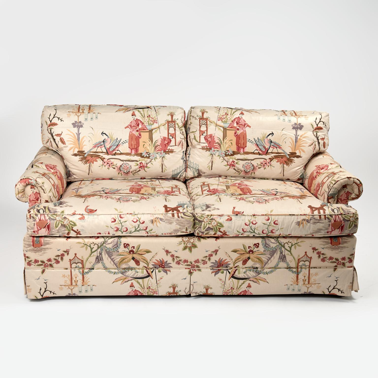 Stand out mid century sofa crafted with loose pillows on the back and seat, classic rolled arms and skirt all around, featuring chinoiserie style upholstery with figures, flowers, and birds. Signed Baker under a cushion.