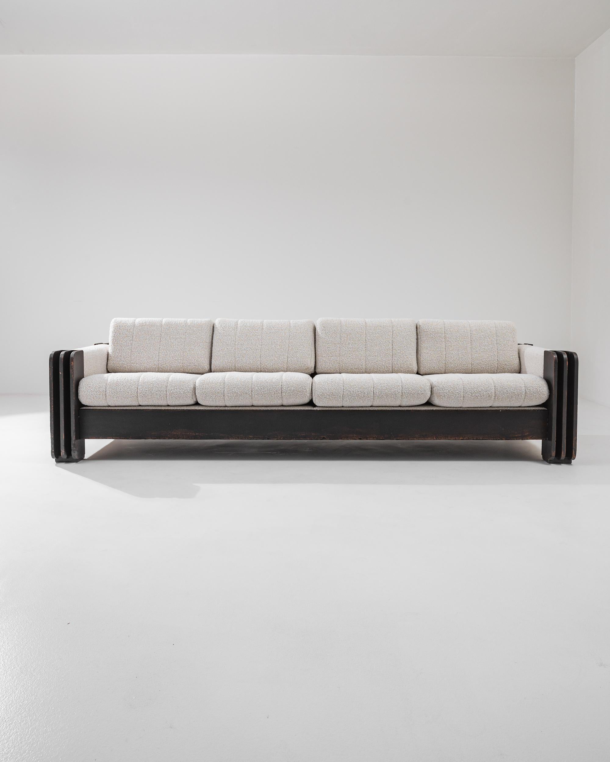 Designed in the 1960’s, this avant-garde four-seater sofa showcases a brutalist base with boldly carved armrests and comfortable upholstered cushions. The juxtaposition of dark patinated wood and the light bouclé upholstery elevates the
