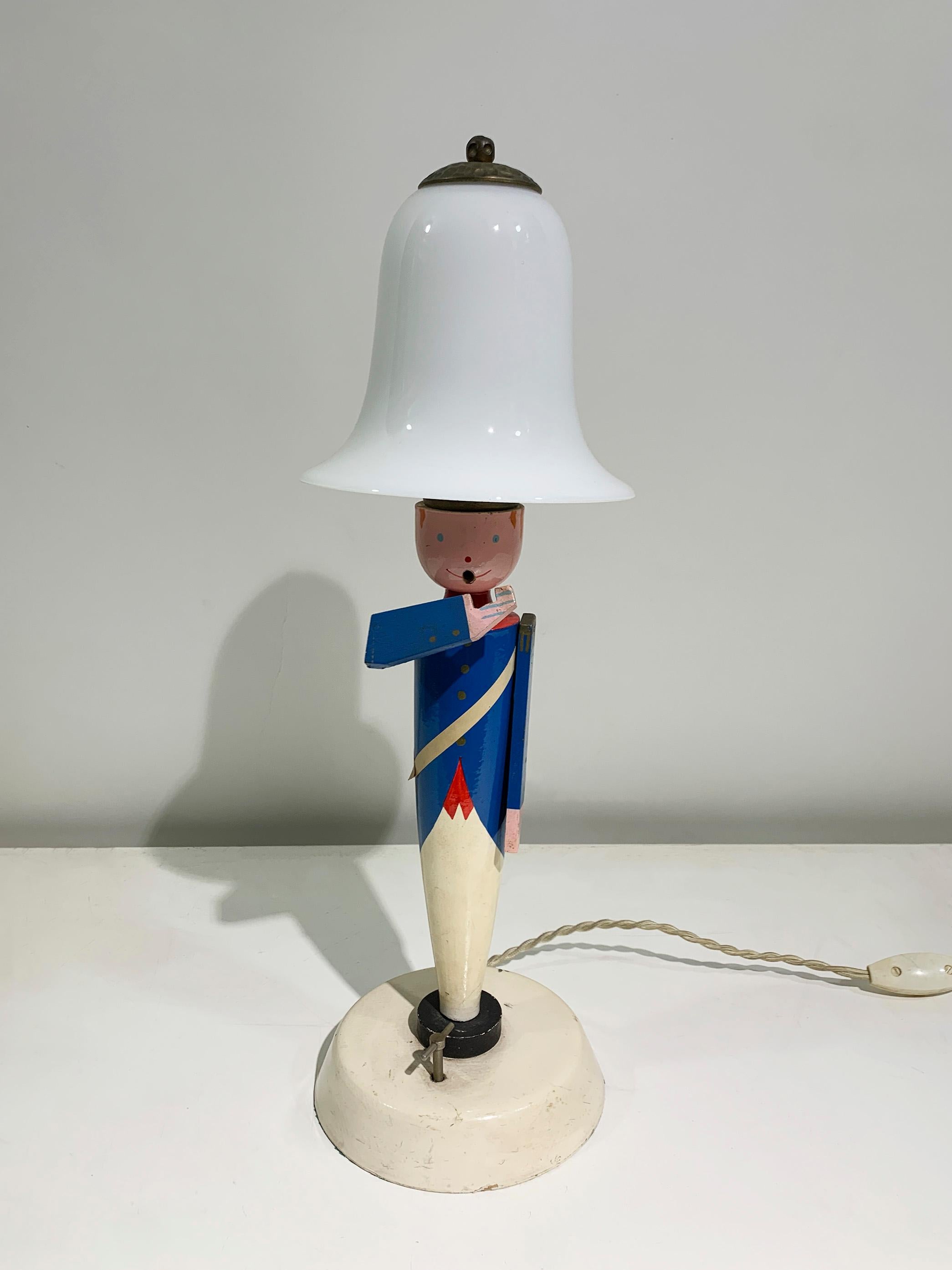Diese skurrile musikalische Tischleuchte von Suzanne Buchion hat ein charmantes Zinnsoldatendesign, wobei der Körper der Figur als Sockel dient. 
Die Farben Rot und Blau sind leuchtend und der Stil dieser Stehlampe ist perfekt für ein Kinderzimmer
