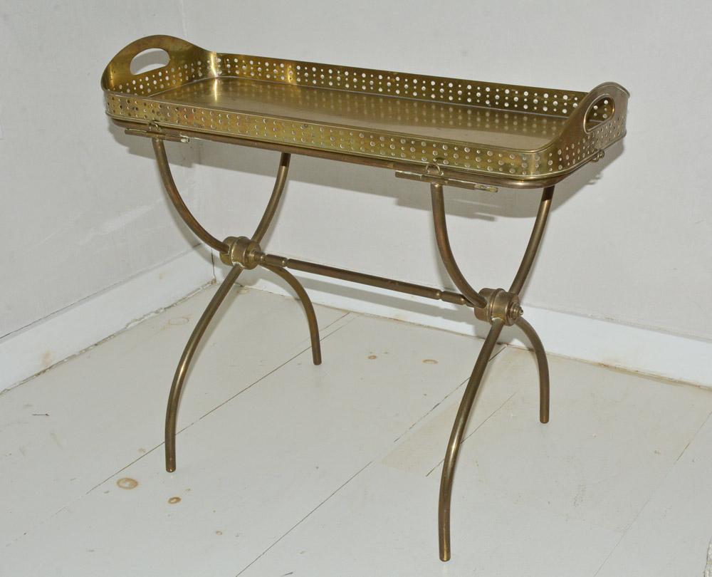 The vintage solid brass gallery tray sits on a tubular curved separate stand of the same material. The tray has end handles and a filigree railing. The stand has six small flanges for securing and stabilizing the tray. Excellent as a bar cart for