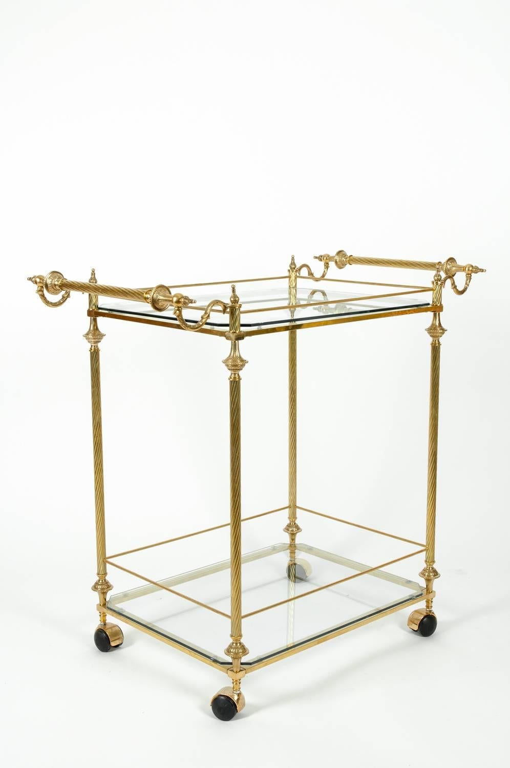 Vintage French solid brass wheeled bar cart / tea trolley with glass shelves and two side handles. The Bar cart / tea trolley is in excellent vintage condition. The cart measure about 33 inches length x 20 inches width x 32 inches high.