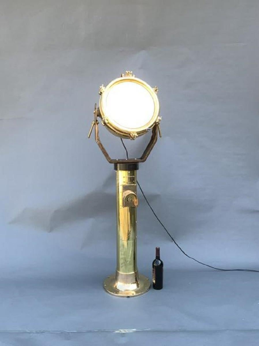 Nautical spotlight. Great piece of industrial lighting. Solid brass and highly polished, fitted to a heavy brass pedestal. Glass lens. Head is fitted to a yoke with adjustment levers to change angle.

Overall Dimensions: Weight is 90 pounds. 62