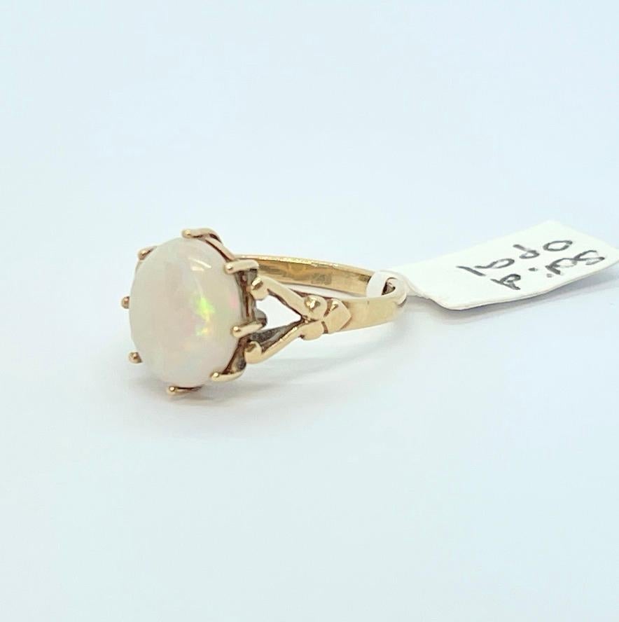 A very pretty, vintage ring featuring a solid, white opal with a light play of colour of green, orange, yellow in the sun.  
The setting is 9ct yellow gold and bears UK hallmarks for Birmingham with the makers mark of CJ.  The date letter is very