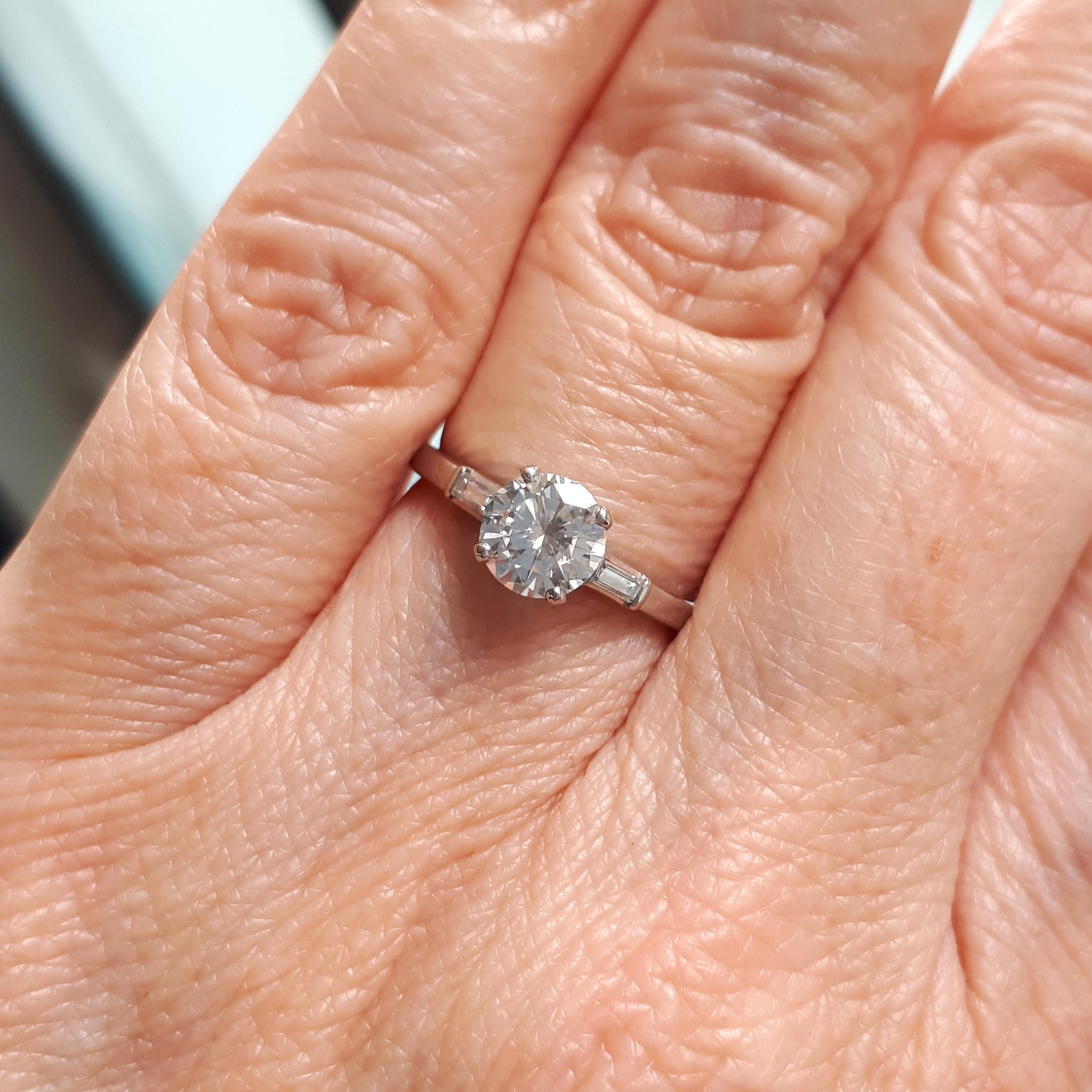 A vintage single stone diamond ring, set with a 0.81 carat, E-F colour, VS1 clarity, round brilliant-cut diamond, in a four claw setting, with baguette-cut diamond set shoulders, mounted in platinum, with a maker's mark for J. & L. Hartzberg,