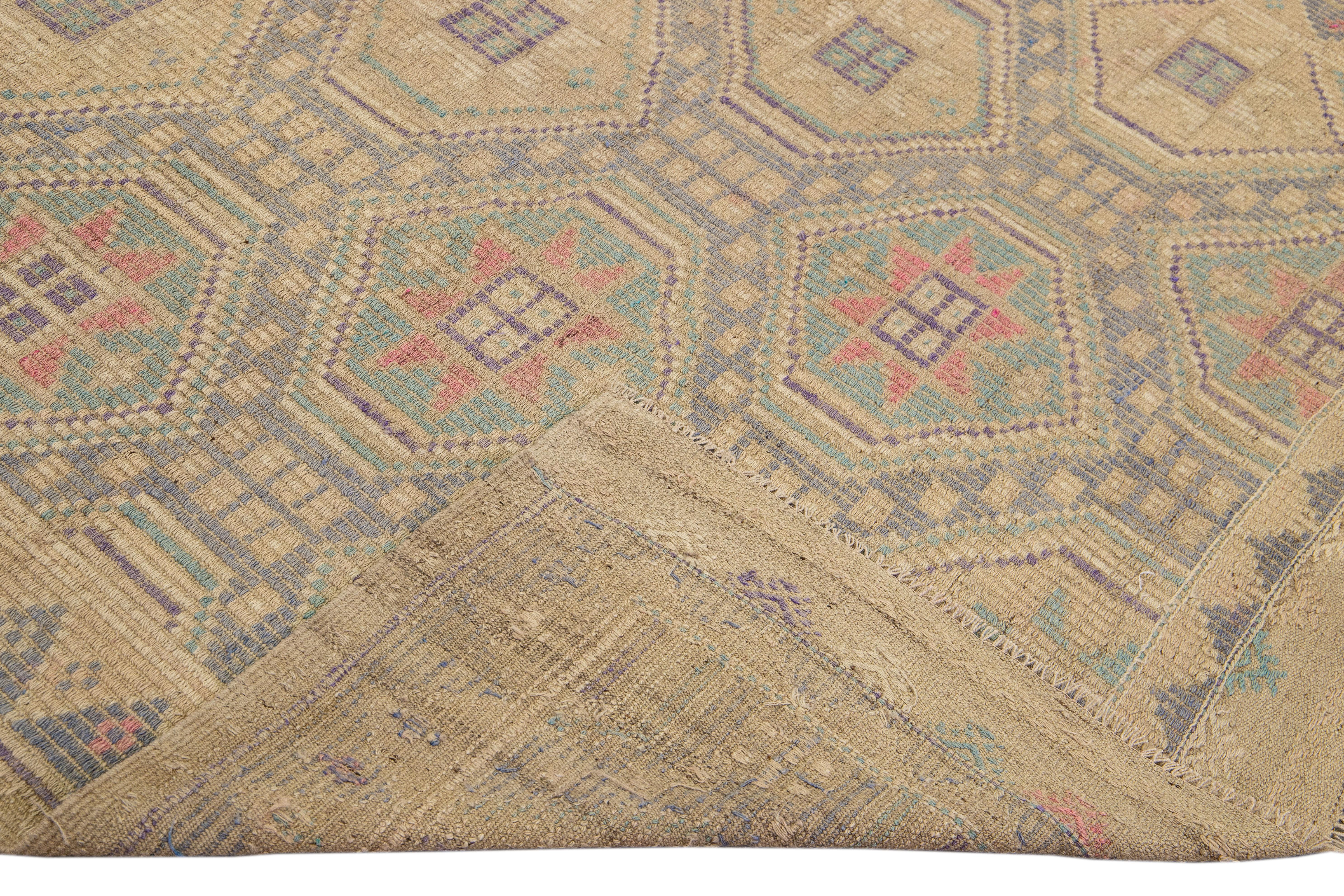 Beautiful vintage Soumak hand-knotted wool rug with a tan field. This piece has purple, blue, and pink accents in a gorgeous all-over geometric medallion motif design with tan fringes.

This rug measures 6'5