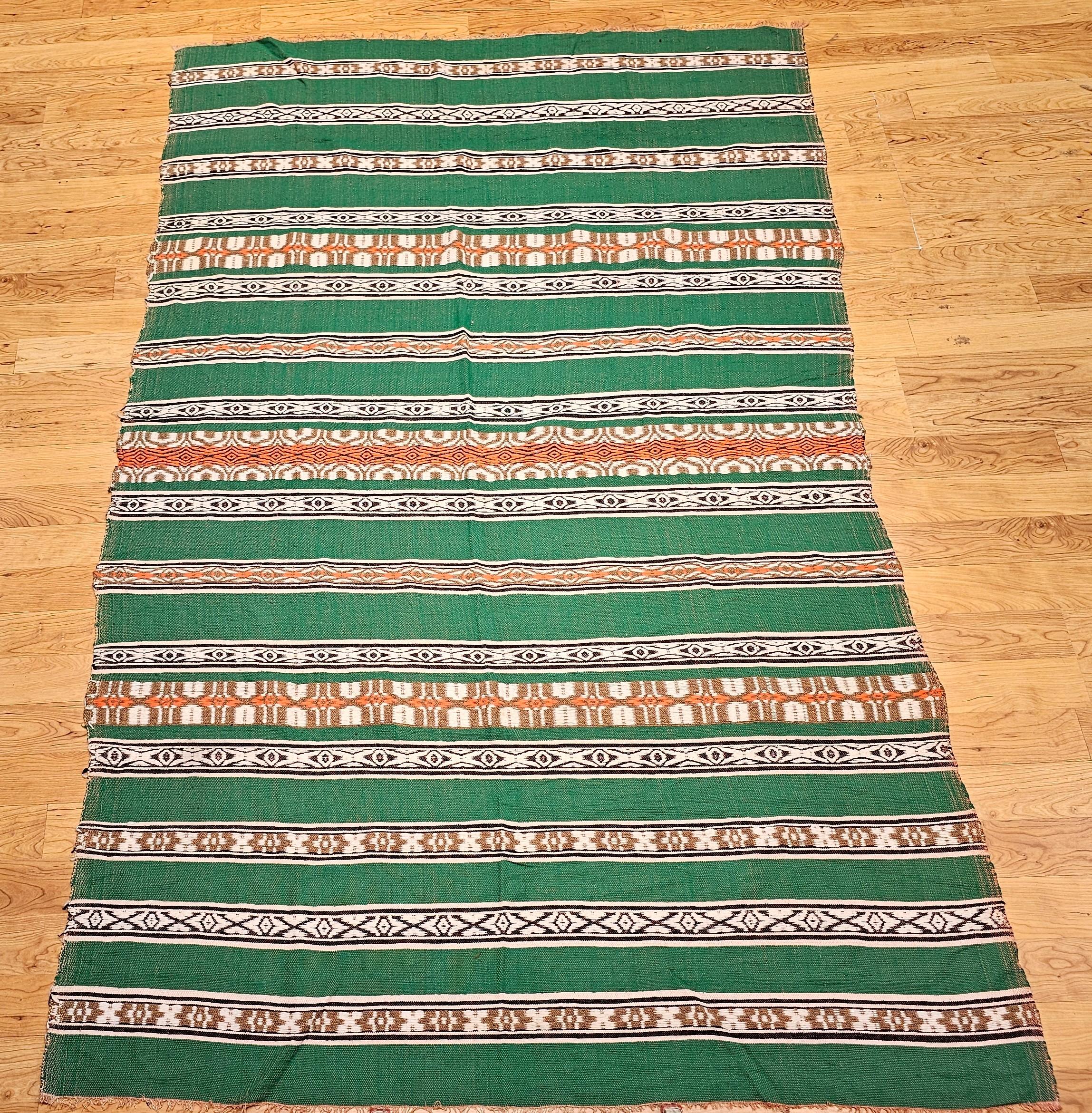 Esta manta vintage del Suroeste, que forma parte de nuestra Colección Americana, muestra maravillosamente la artesanía tradicional mexicana con un atemporal dibujo de bandas alternas en verde, marfil, marrón, naranja y negro. Tejida en México