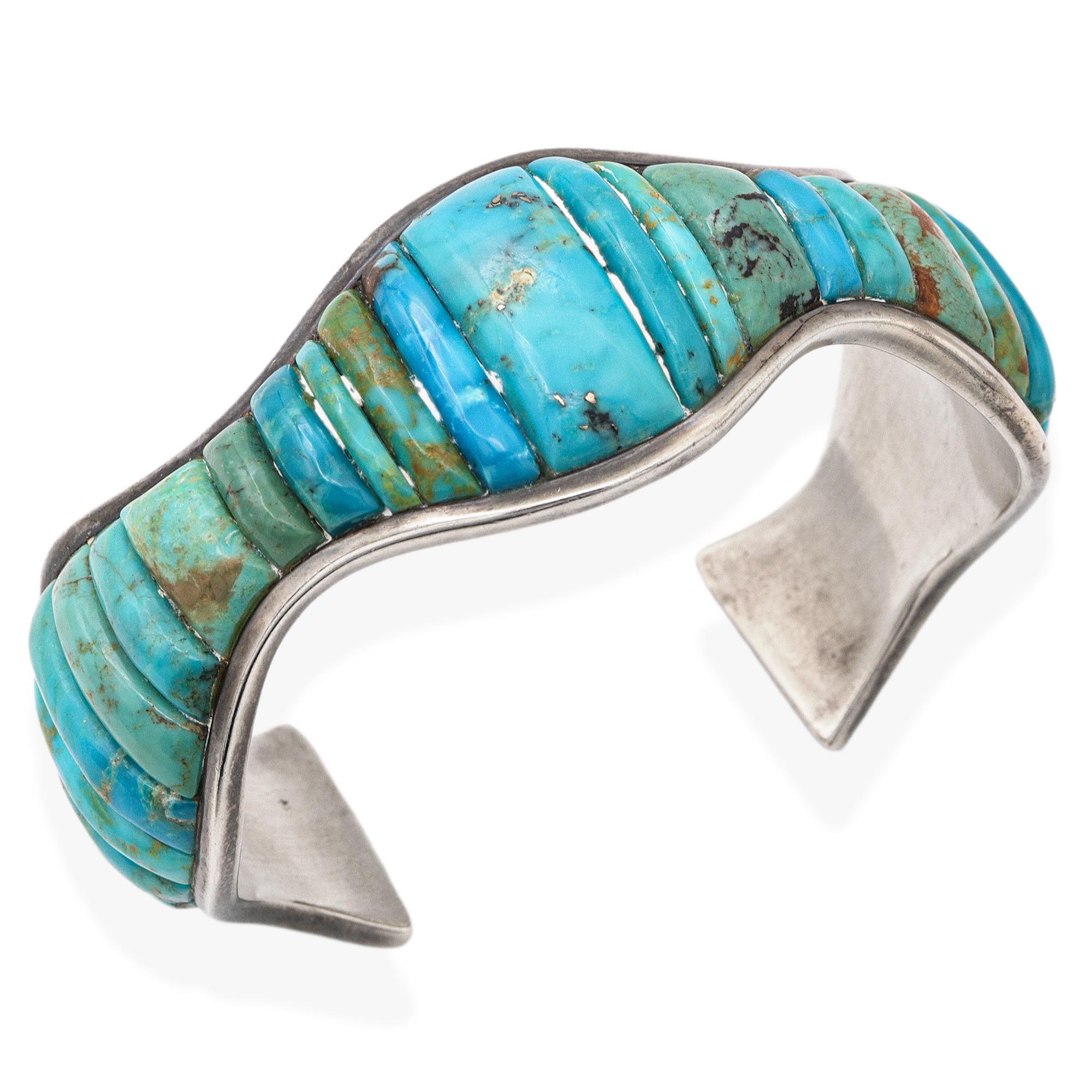 This vintage Southwestern cuff bracelet showcases a bold and sculptural design, crafted in sterling silver and set with richly hued turquoise stones. The cuff features a wave-like form accented by hand-carved turquoise tabs in varying shades of blue