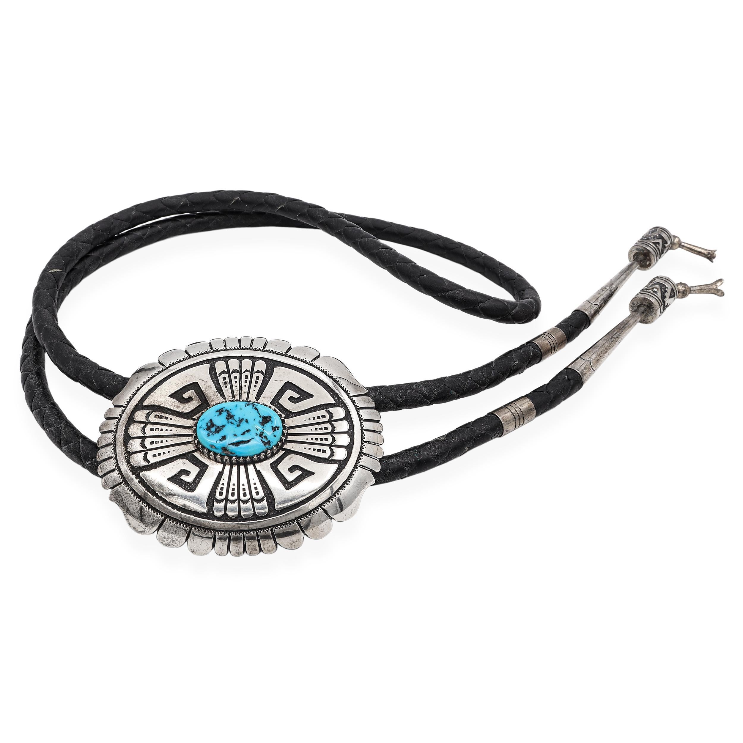 Un'eccezionale cravatta bolo in argento sterling Navajo realizzata a mano dal rinomato argentiere Thomas Singer, con un sorprendente cabochon di turchese incastonato in un'intricata slitta in stile concho. Il design audace incorpora motivi
