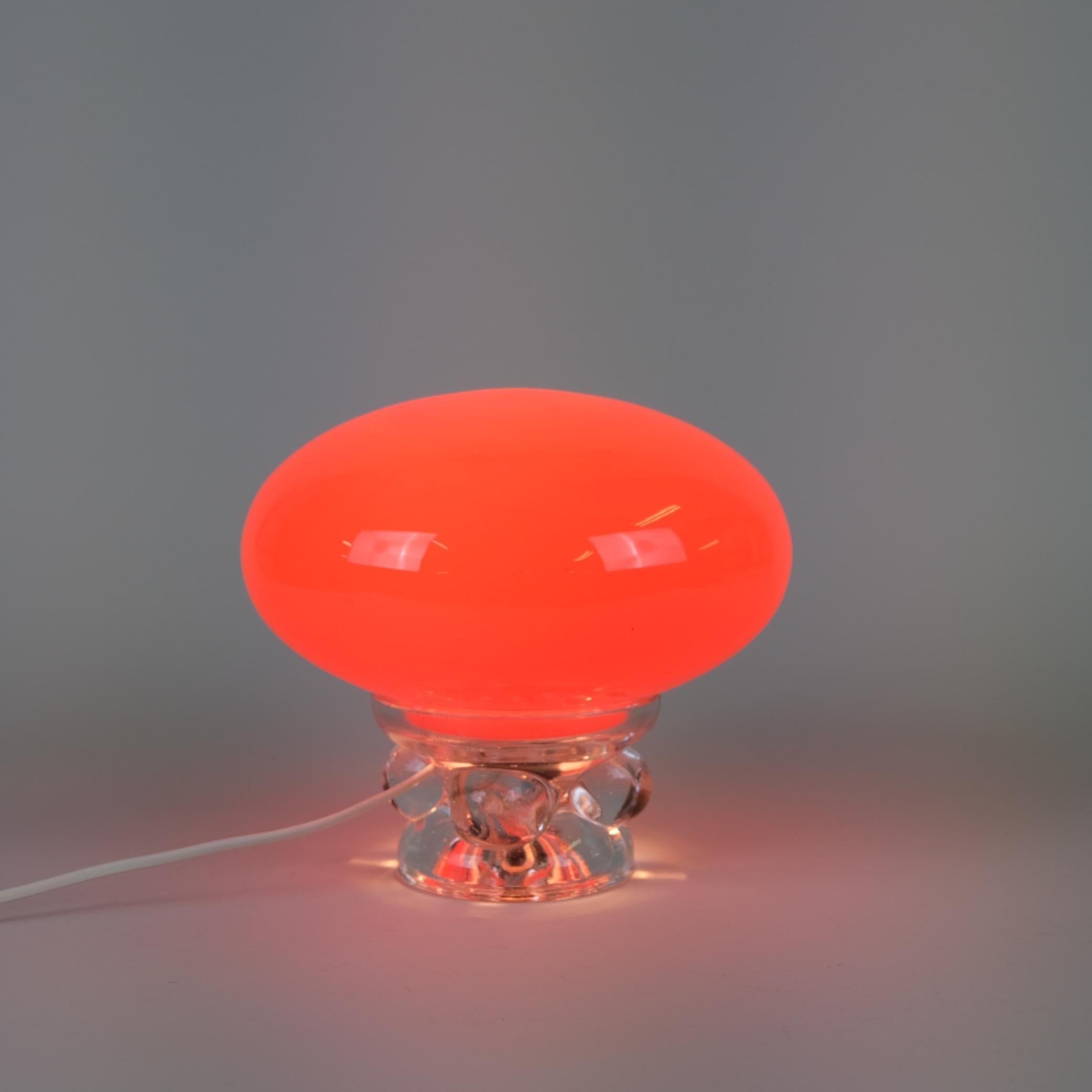 Lampe de table vintage en verre à champignon rouge de l'ère spatiale. Cette lampe funky convient aux intérieurs colorés, d'époque et rétro grâce à sa couleur rouge vibrante, presque orange, surtout lorsqu'elle est allumée. La lampe est composée