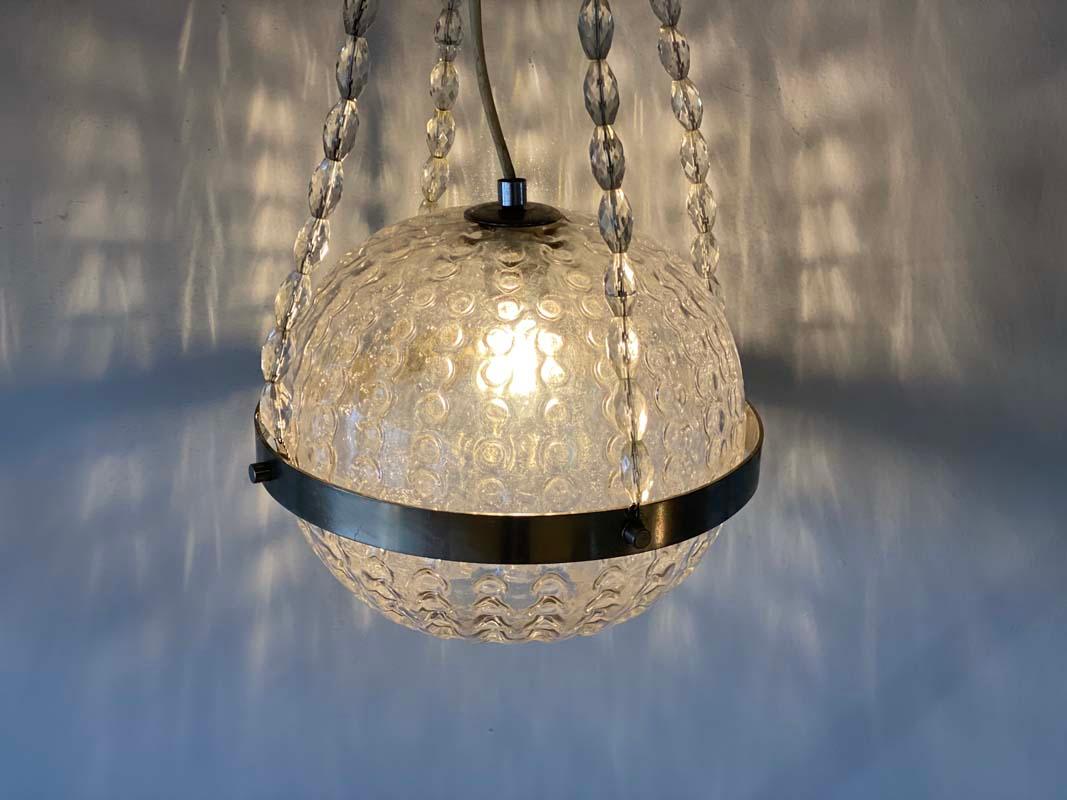 Cette lampe suspendue est originaire d'Allemagne et date des années 1970. Il est composé de pièces en verre, en métal et en plastique. La boule de verre est maintenue par un anneau en métal et est suspendue à 3 chaînes de perles en forme de diamant.