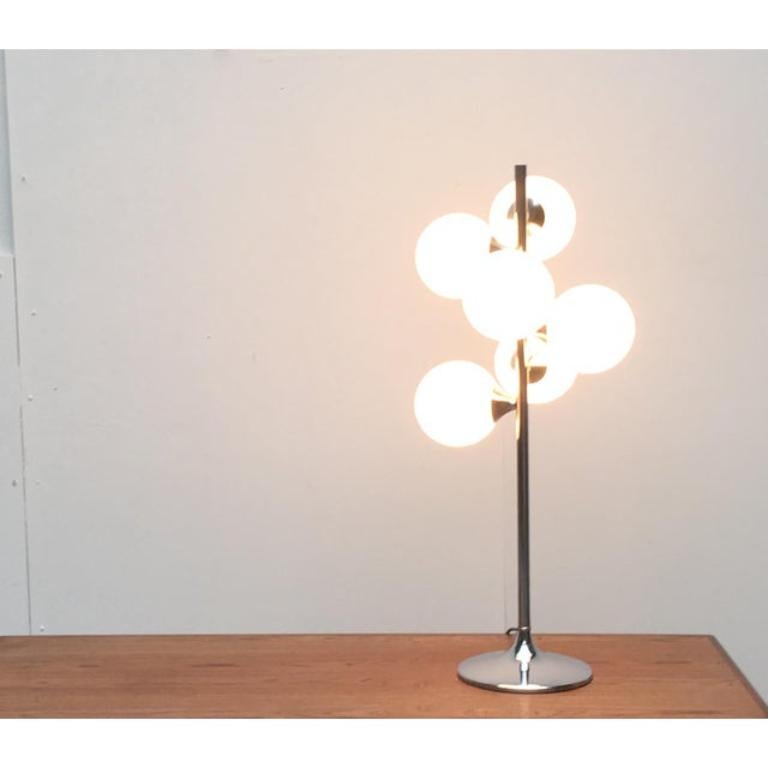 Il s'agit d'une imposante lampe de table de l'ère spatiale avec six boules de verre. Les boules de diffusion 6 en verre opale sont disposées à différentes hauteurs radialement autour du pied central. Le pied chromé est conçu en forme de tulipe. Les