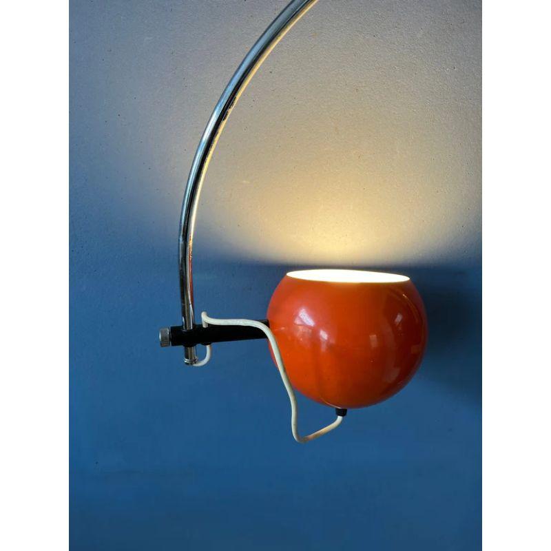A classic arc wall lamp with orange eyeball shade from the Dutch brand Herda. The shade can be turned in any direction desirable and positioned inside or outside the arc. The lamp has a switch build into the cable. The lamp requires an E27