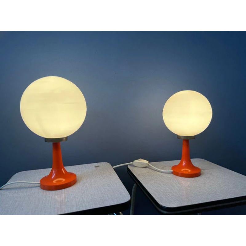 A set of glass-made pop-art table lamps, reminds of Carlo Nason. The glass shade is white and the base orange/red. The lamps require E14 lightbulbs and currently have EU-plugs.

Dimensions:
ø Shades: 14 cm
Height: 24 cm

Condition: Excellent.