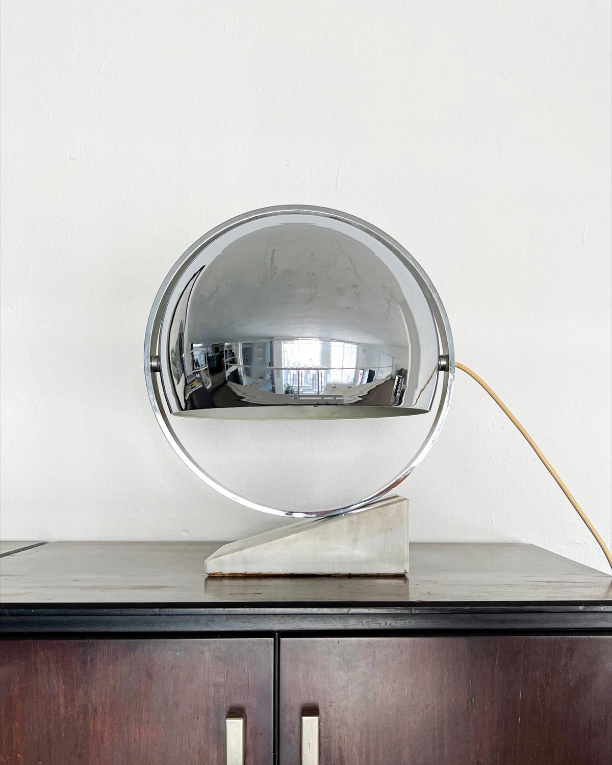 Nous proposons à la vente une lampe de table vintage de l'âge de l'espace fabriquée en Italie vers le milieu des années 1960. Elle repose sur une base triangulaire en marbre blanc de Steele et possède un cadre rond en acier inoxydable supportant un