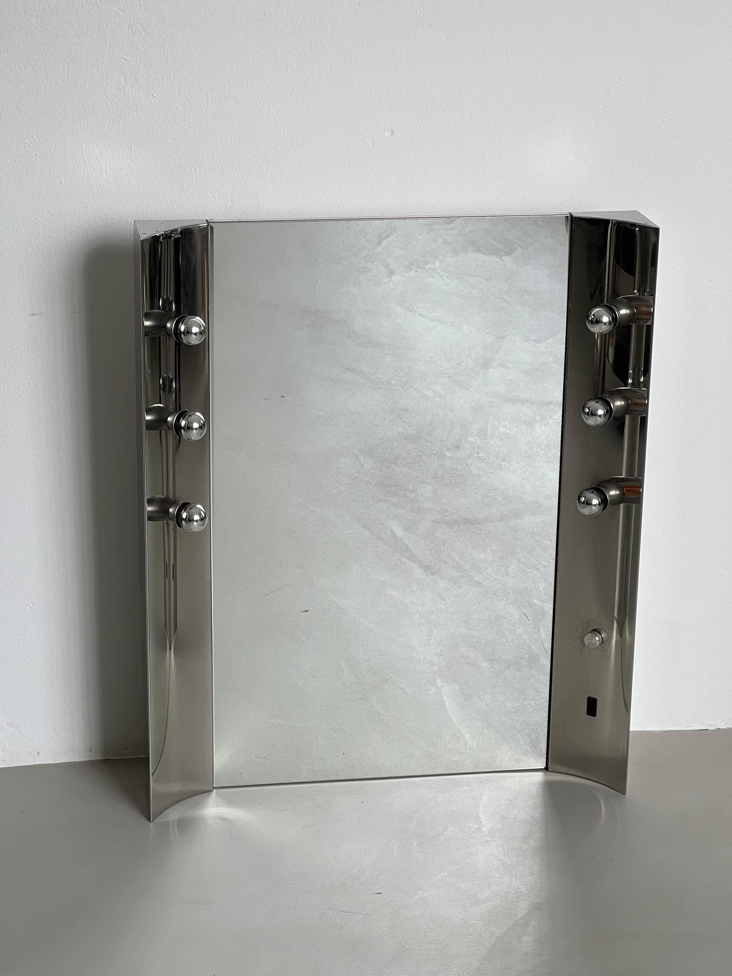 Offered for sale is a vintage Space Age vanity mirror, with six integrated light bulbs and a plug to connect a razor or hair dryer. The piece is big, and is suitable both for a bathroom and a powder/changing room. Its inward rounded sides make it